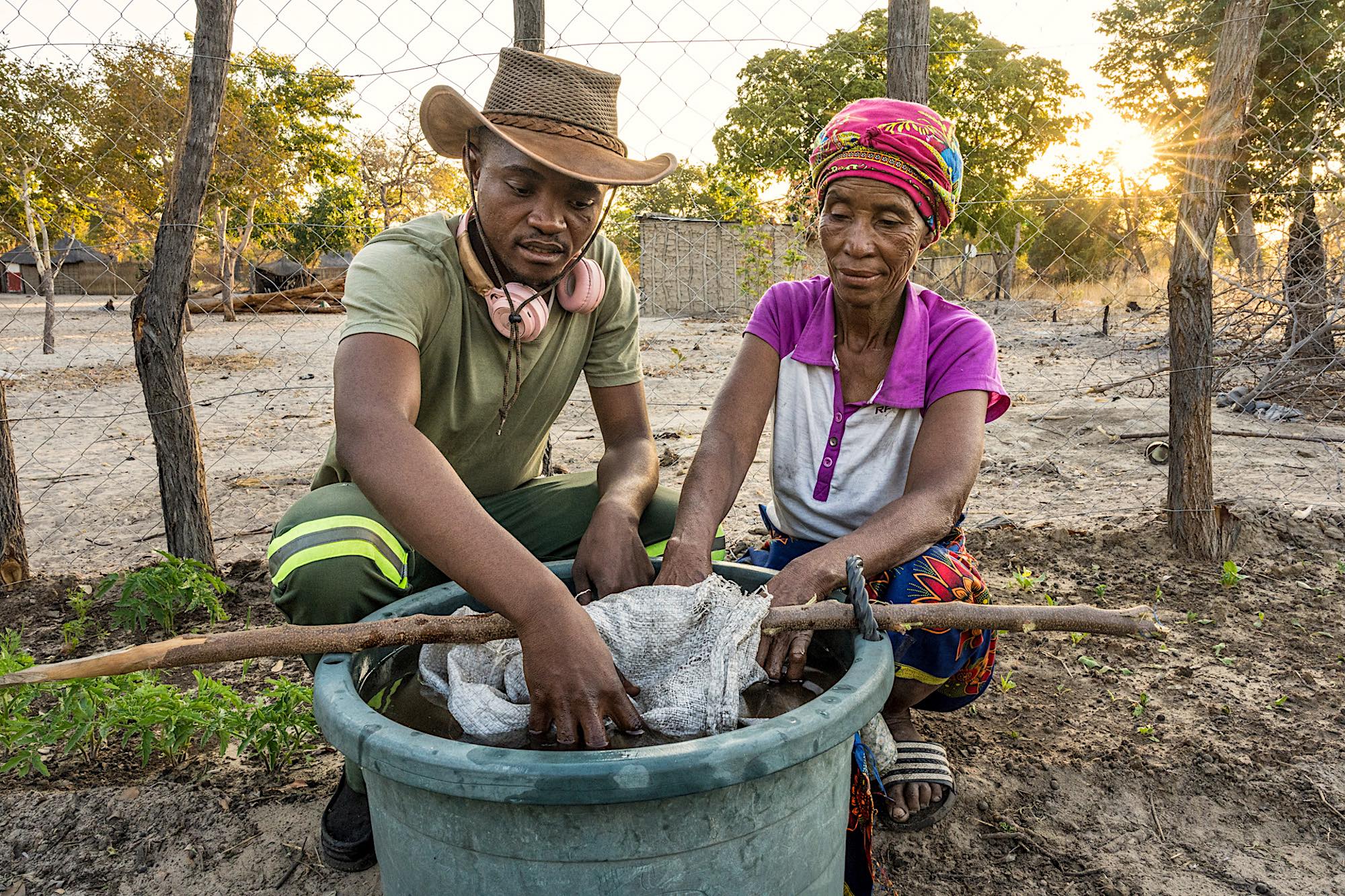 A man and a woman squat down while stirring a bucket.