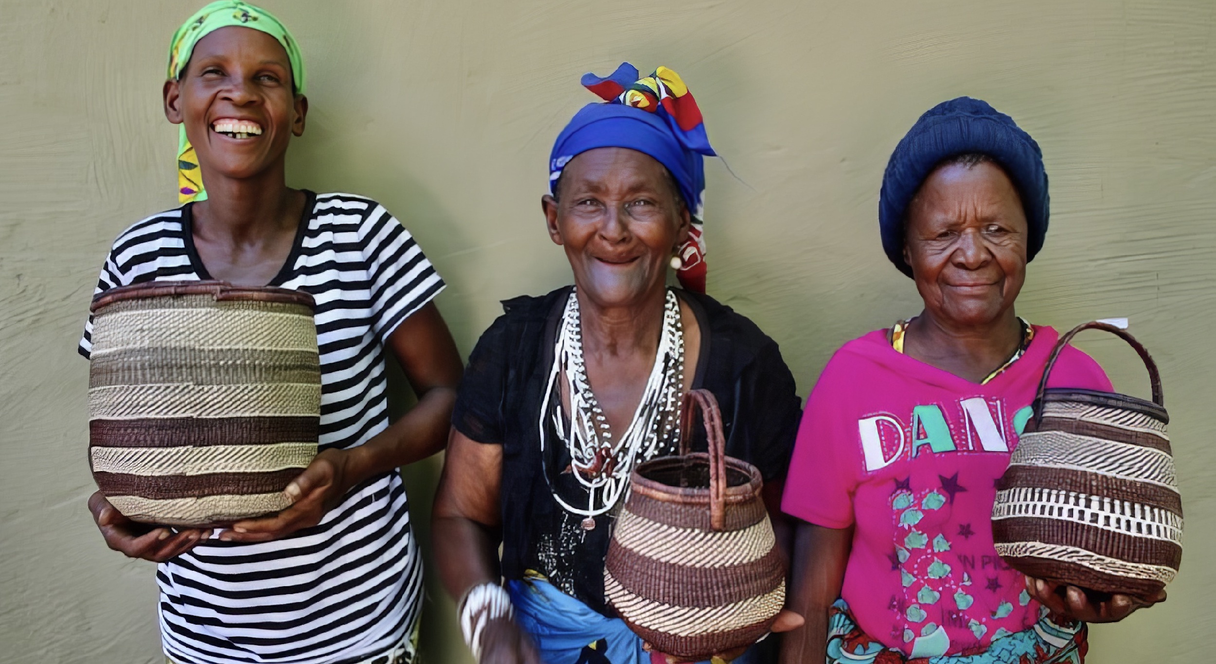 Three colourfully dressed San ladies holding woven baskets and smiling at the camera.