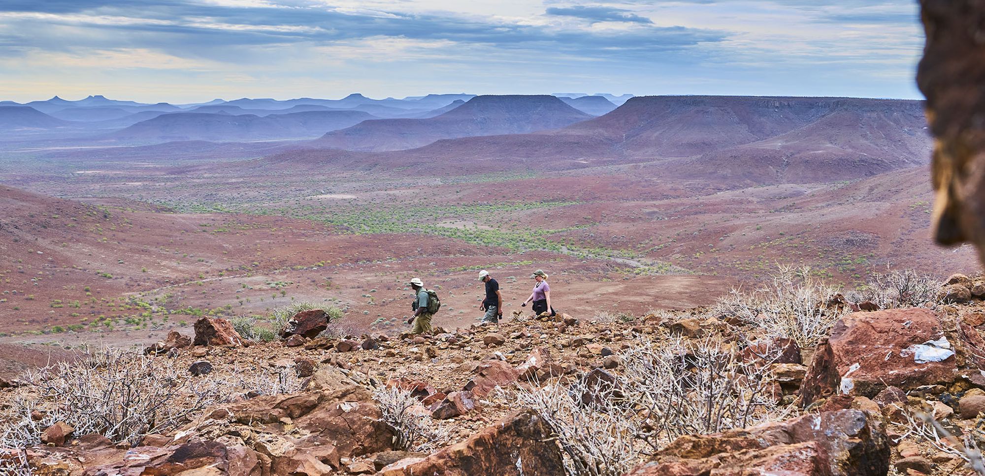 A guide leads three tourists along a rocky trail overlooking the stunning scenery of northern Namibia.