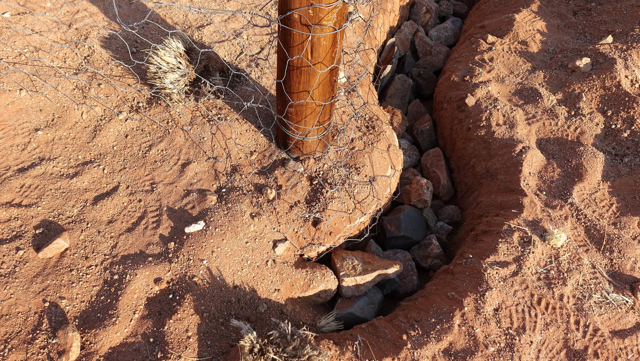 Close-up view of a fence and post embedded deep in the ground, and rocks used to ensure predators cannot dig underneath.