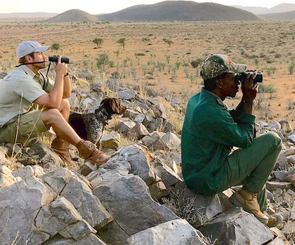 A hunter, his guide, and a dog, stare into the distance looking for wildlife.