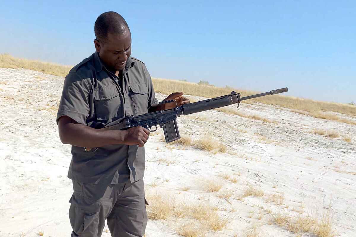 Johannes Ikela standing in Etosha and holding his R1 rifle.
