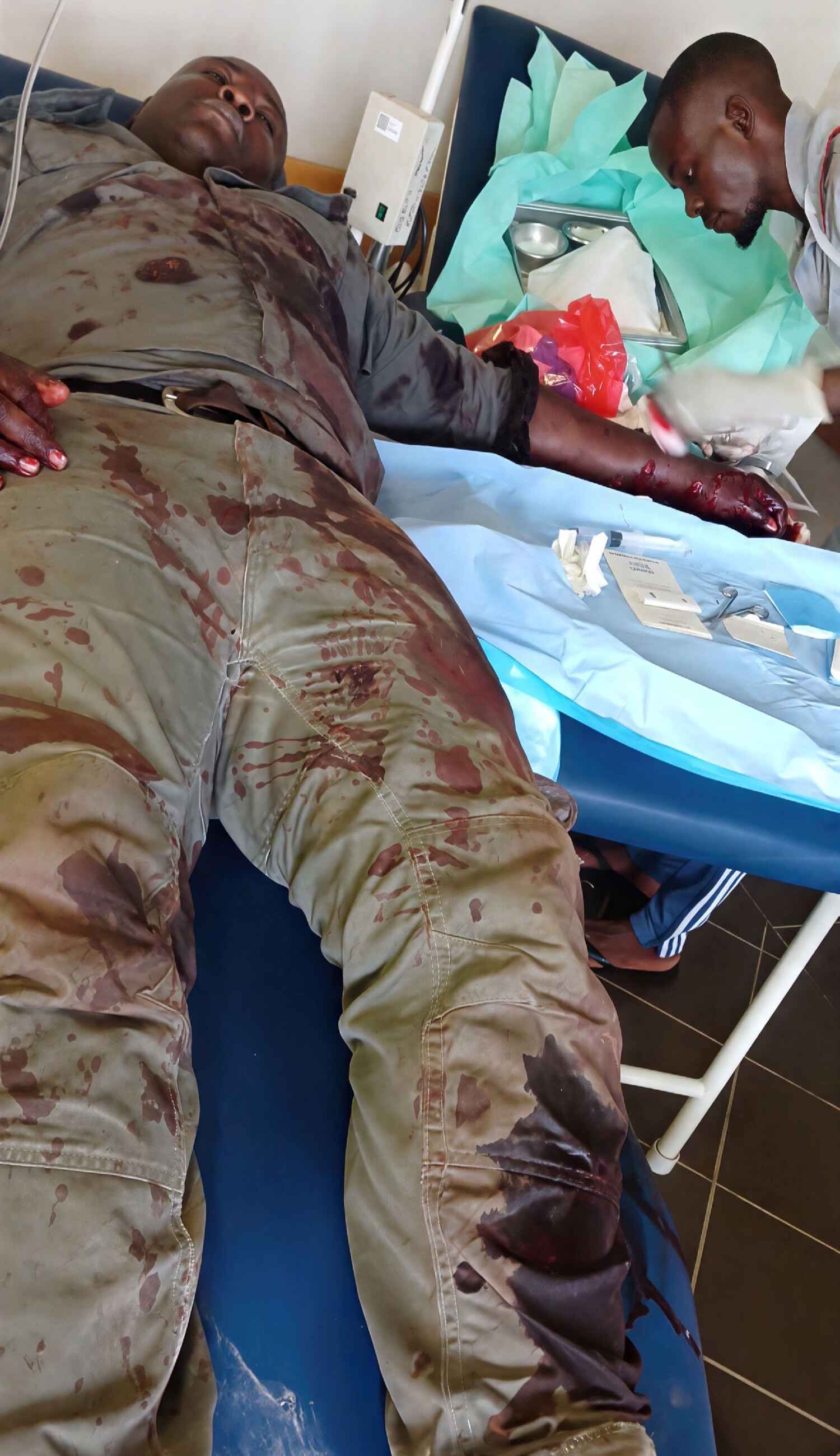 Johannes lies in a hospital bed still wearing his bloodied uniform.