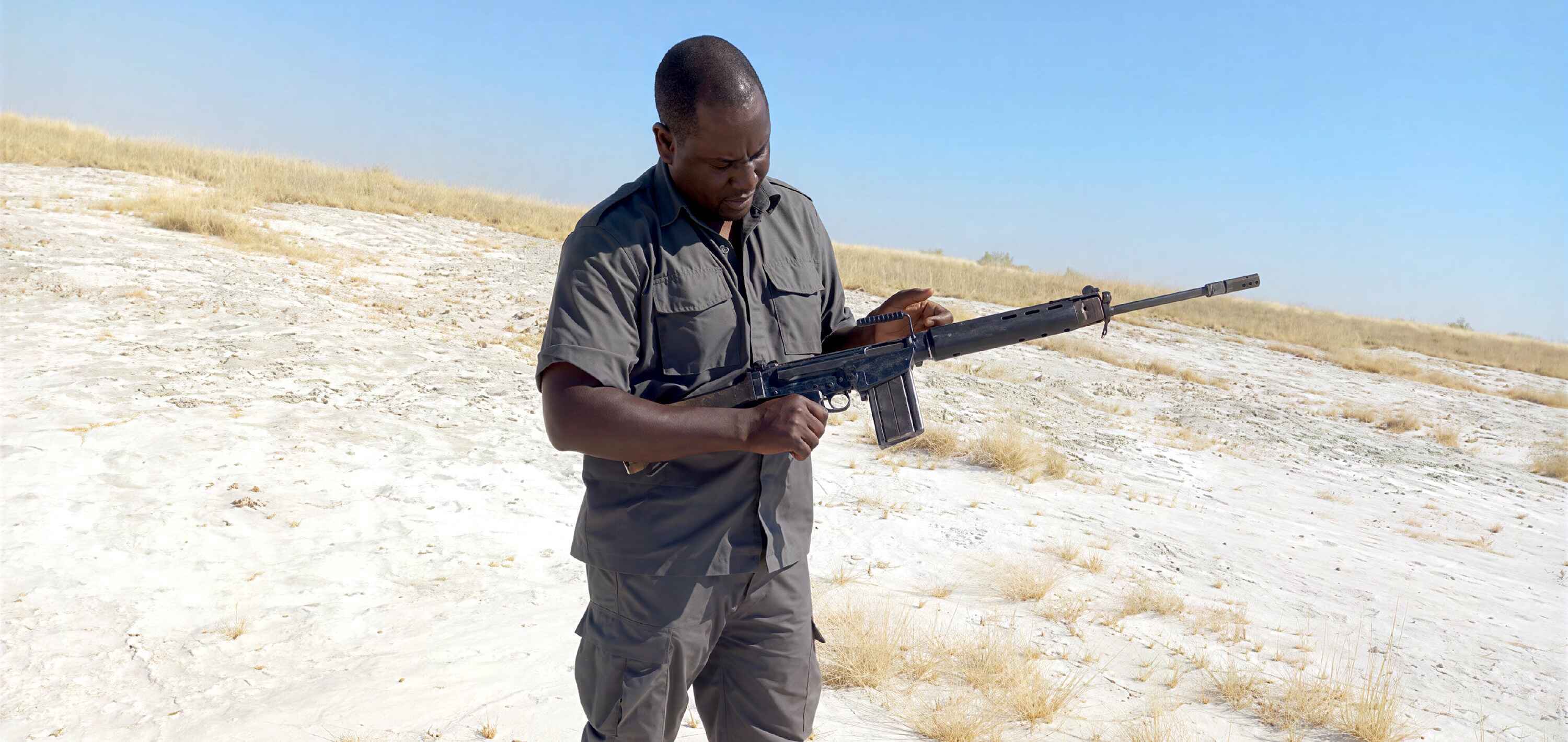 Johannes Ikela standing in Etosha and holding his R1 rifle.