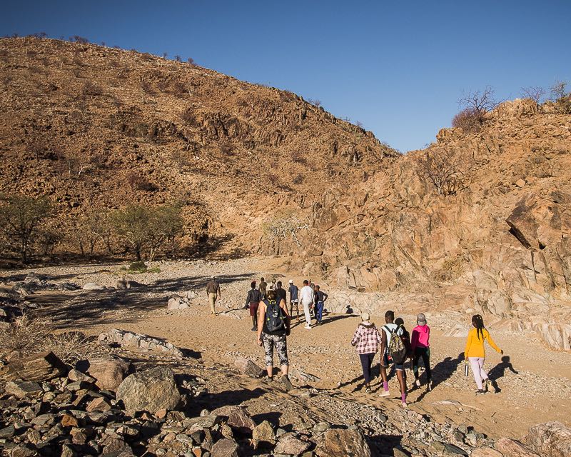 The guides and children walk down a dry riverbed.