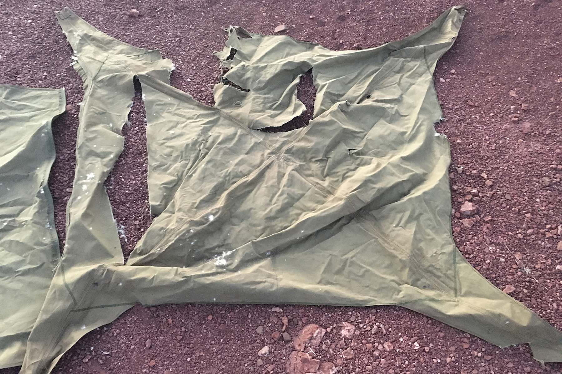 The shredded remains of a tent lie on the stony ground.