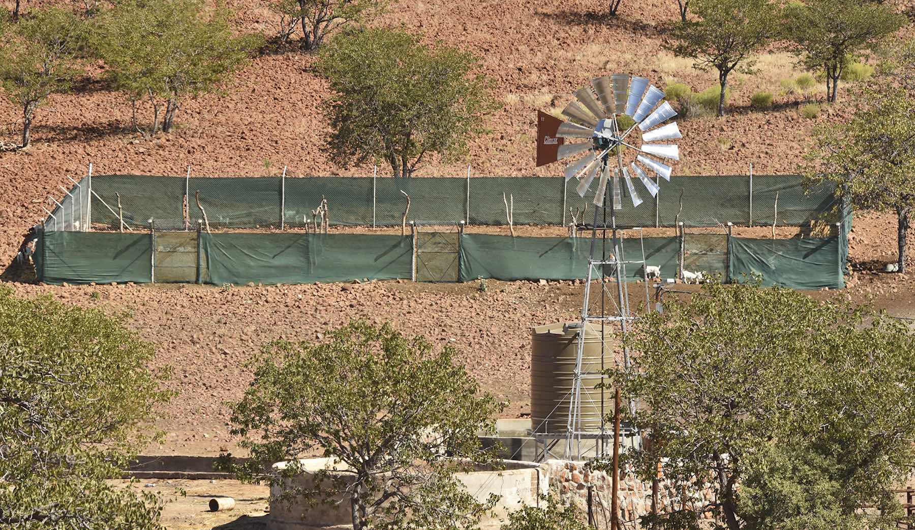 A waterpoint and a metal-and-shade cloth animal enclosure (kraal) in a rocky environment.