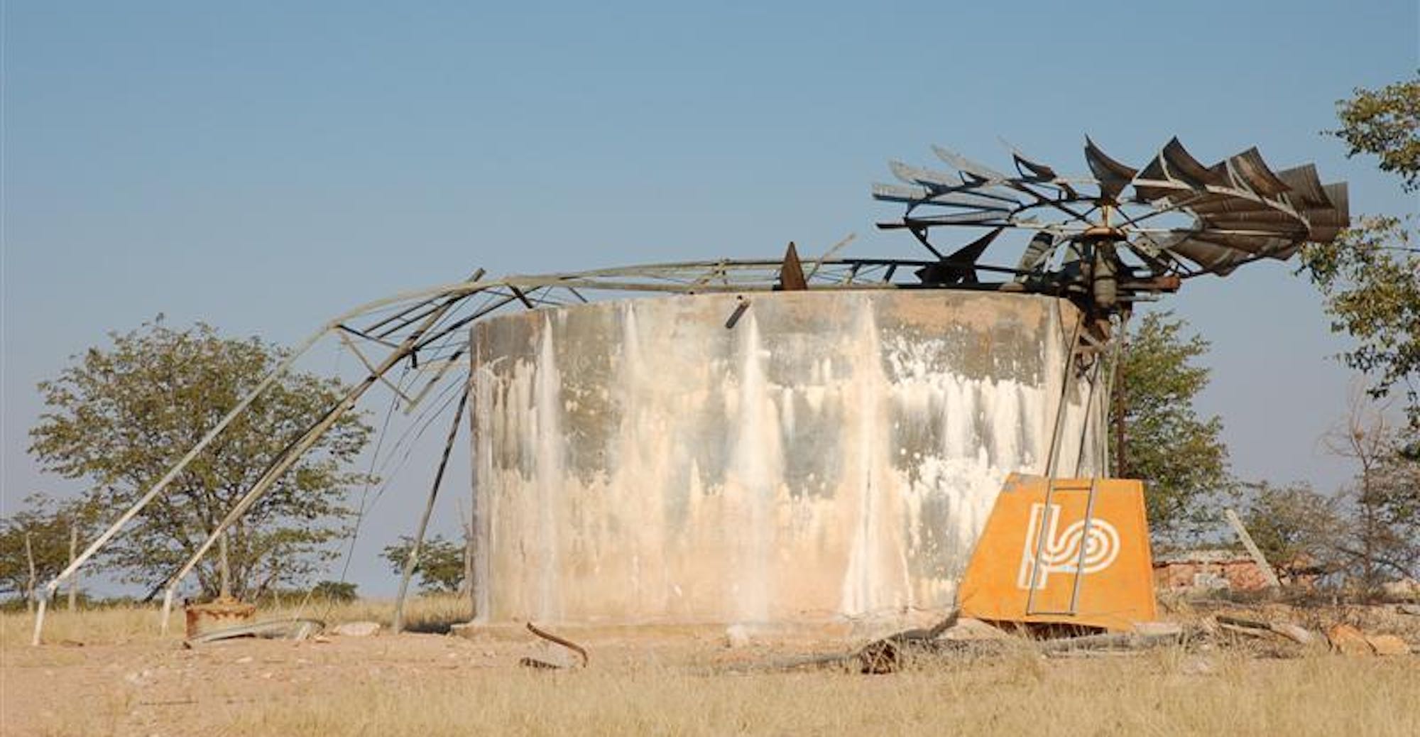 The broken remains of a windmill used to pump water from a borehole lies horizontally across a cement water tank.