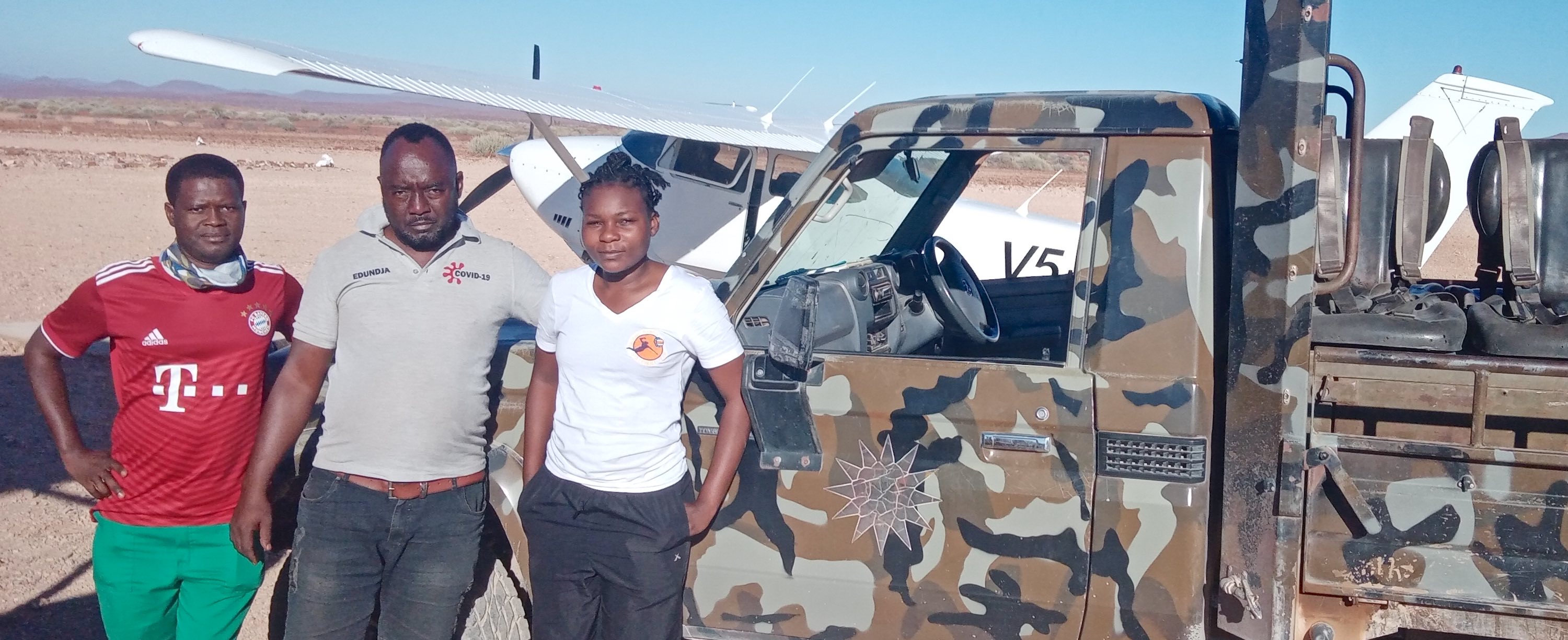 Three people, and a camo coloured vehicle in front of a plane.
