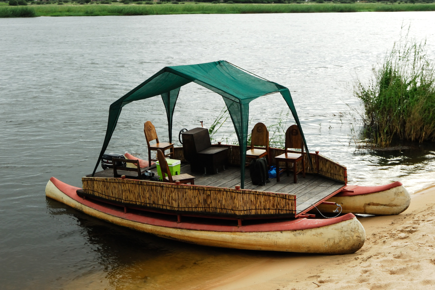A simple boat with chairs and a shade covering that is built on top of a pair of canoes.