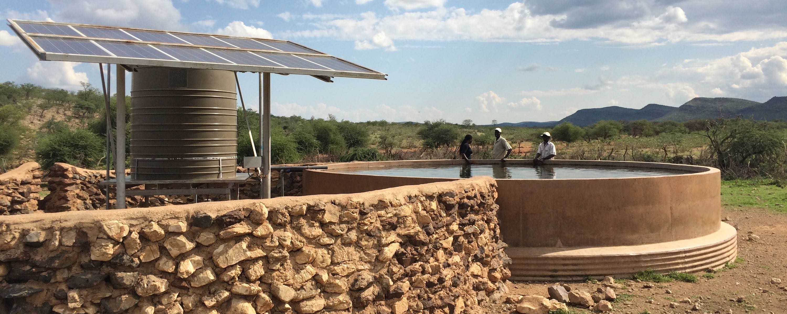 A stone wall protects the solar pump and tank that are next to a cement water point.