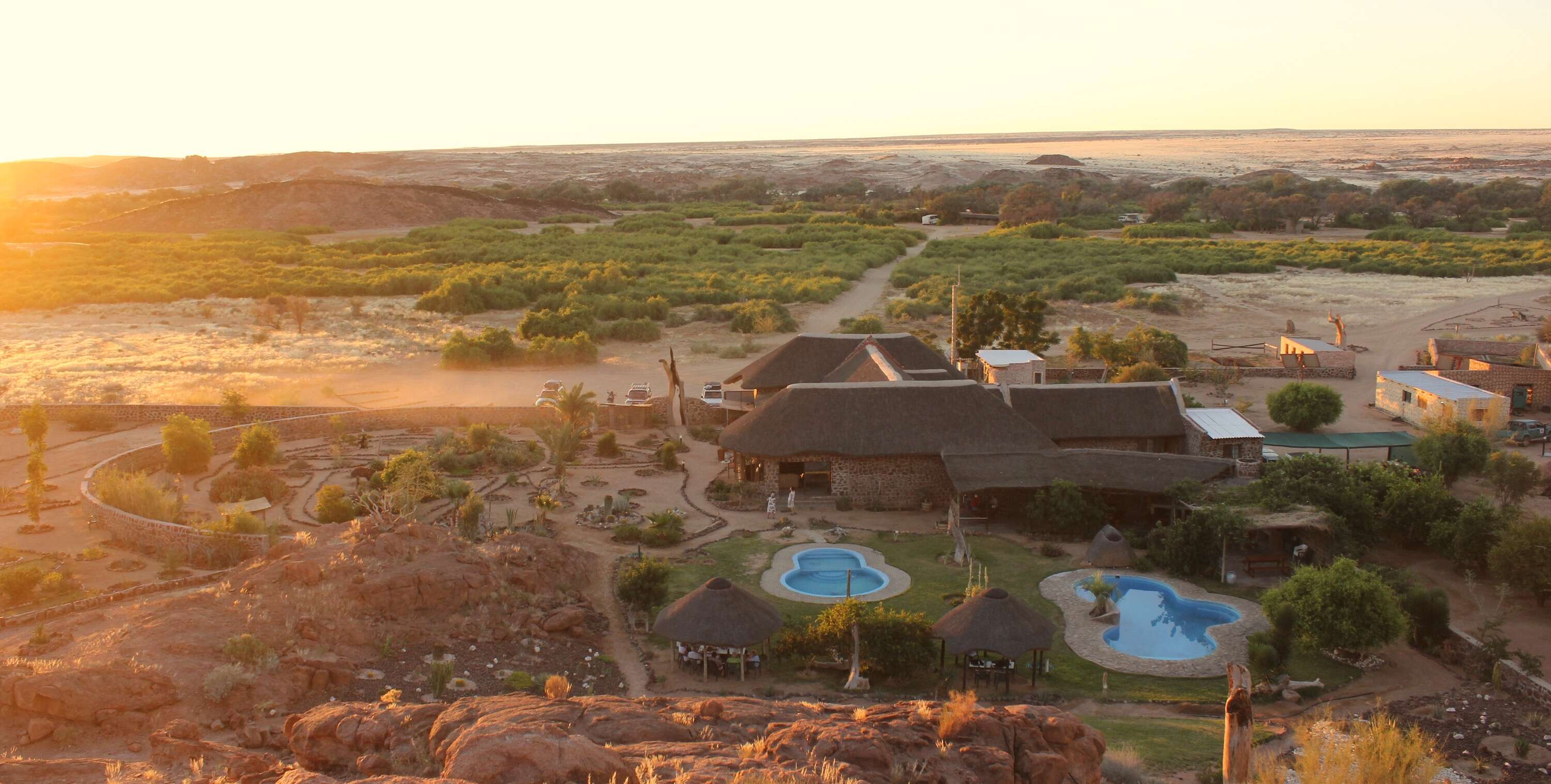 Looking down on a large lodge with two swimming pools while the sun is setting.