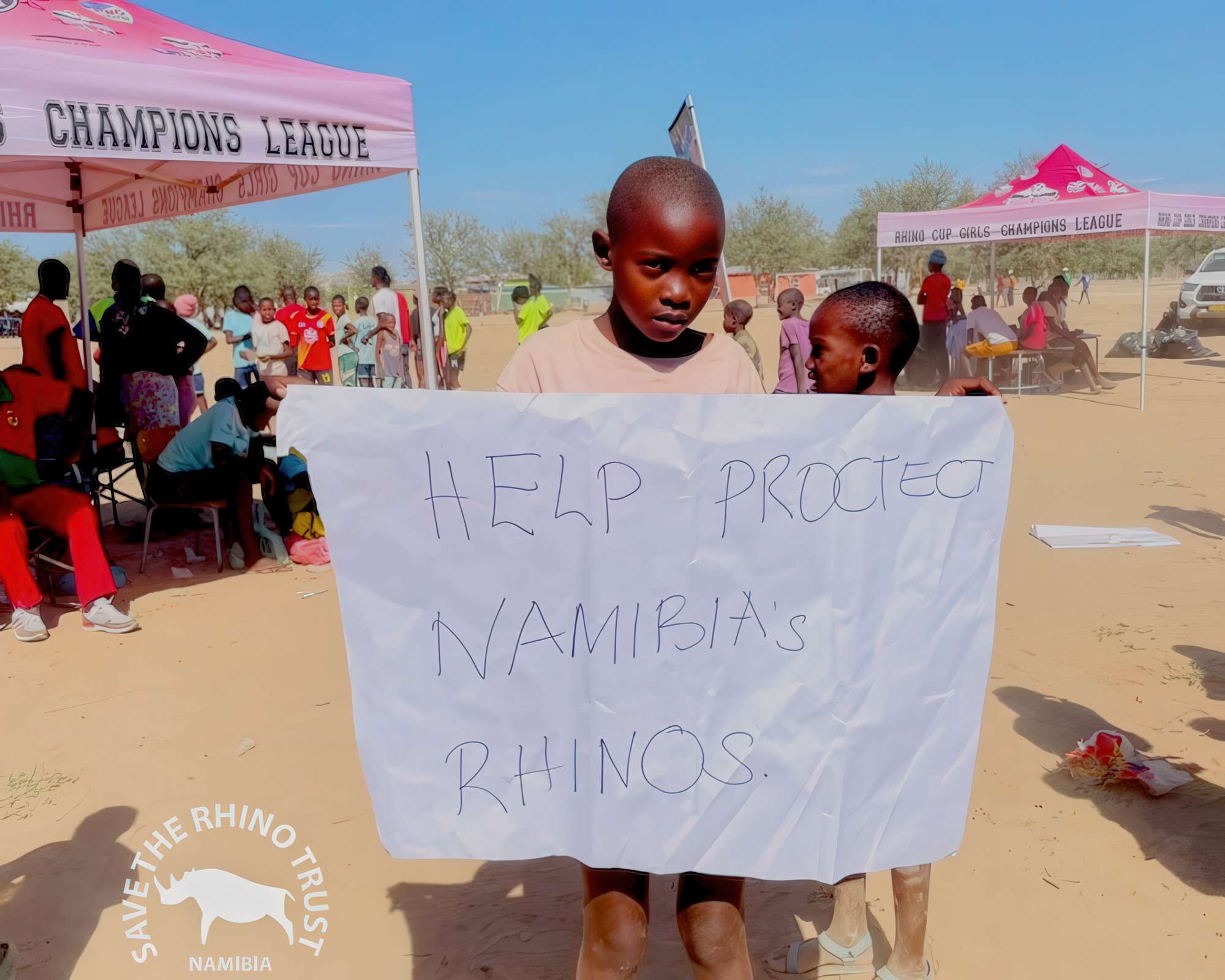 A young child holds a banner that reads: Help protect Namibia's rhinos.