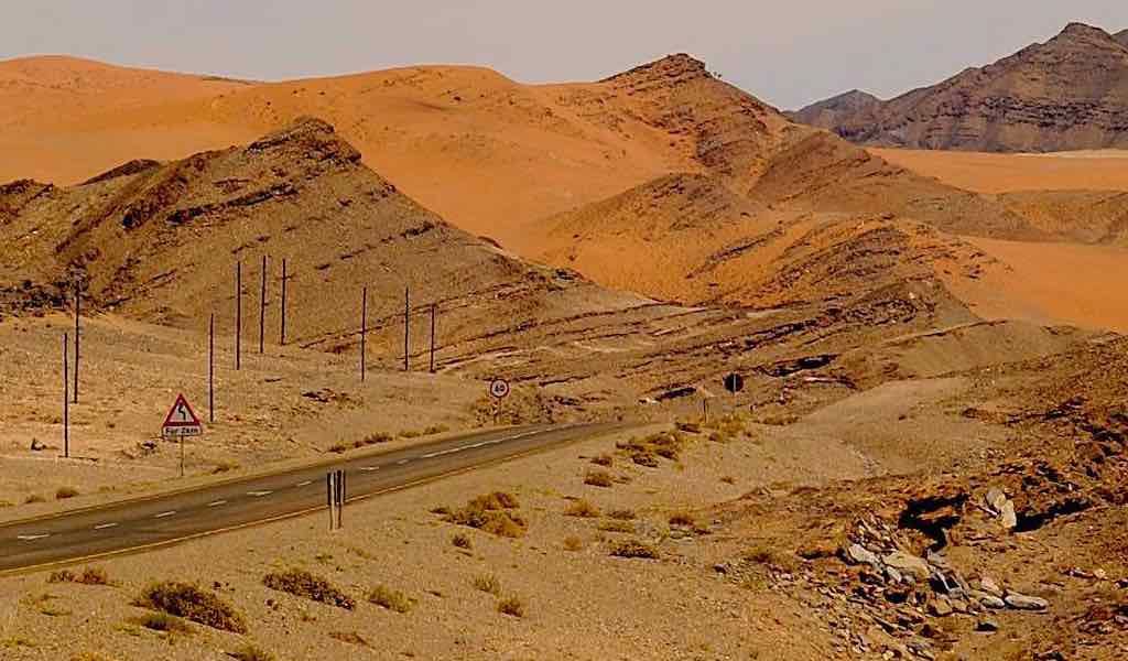 A road and pylons cut through a mountainous and desert environment.