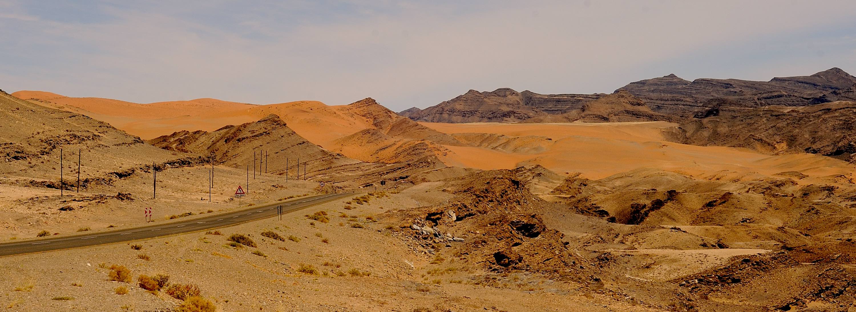 A road and pylons cut through a mountainous and desert environment..
