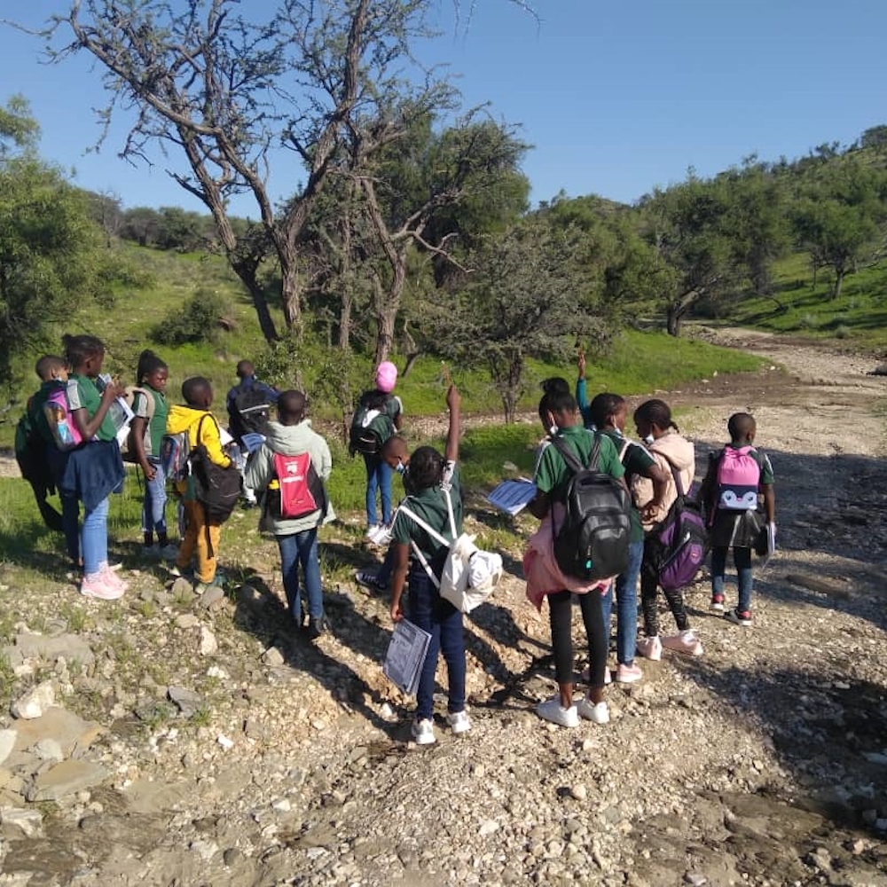 A group of people walking on a trail by a dry riverbed.