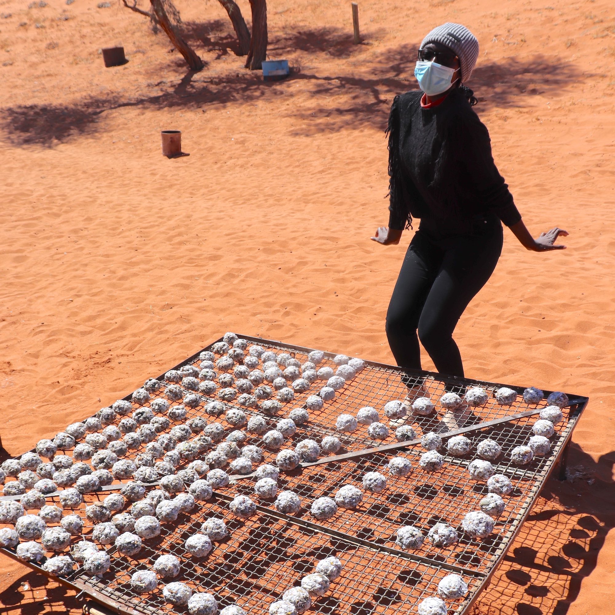 A woman poses next to a mesh grid with fireballs drying on it.