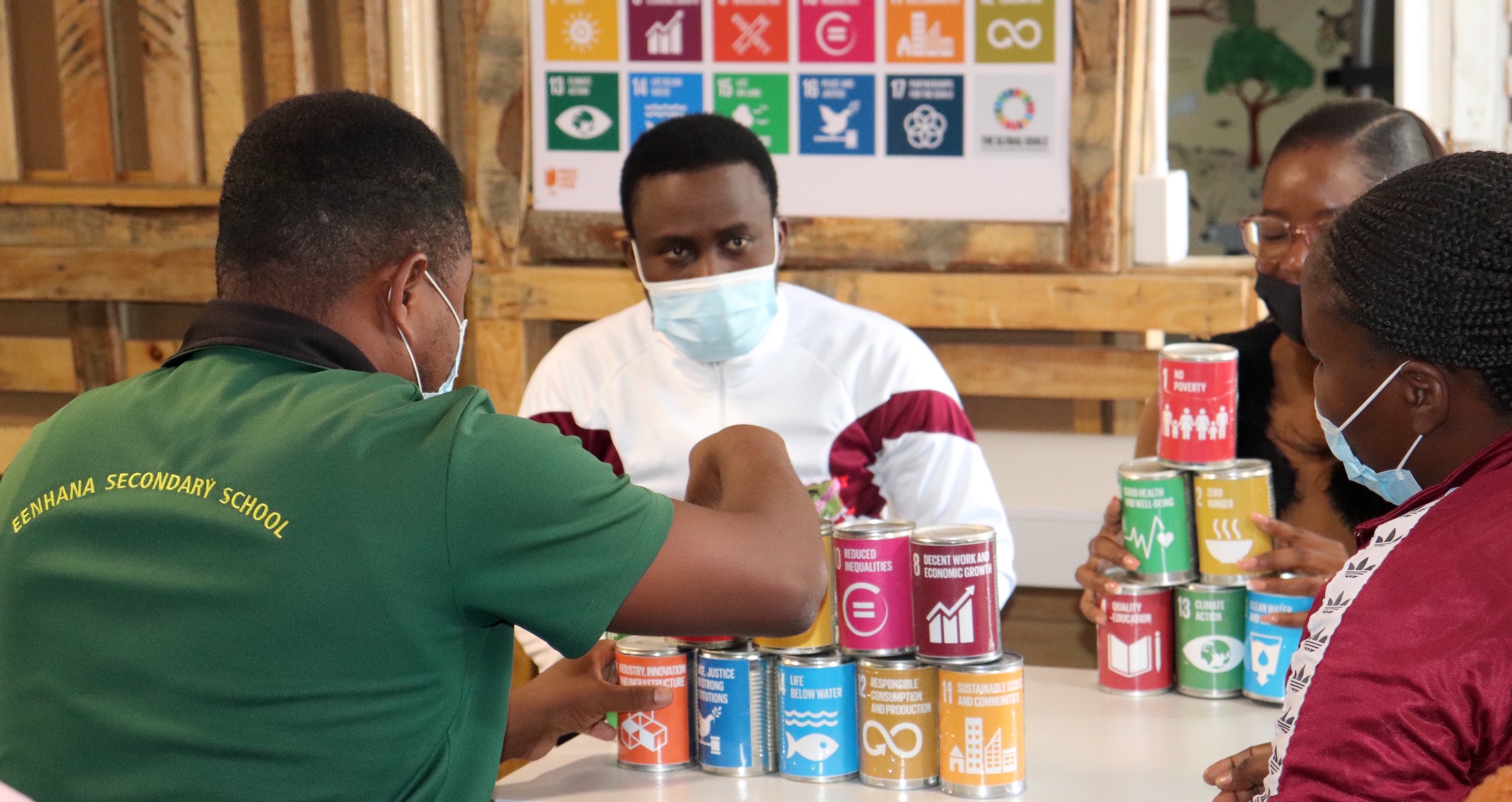 Four people sit around a table while they stack tin cans labelled with various SDGs.