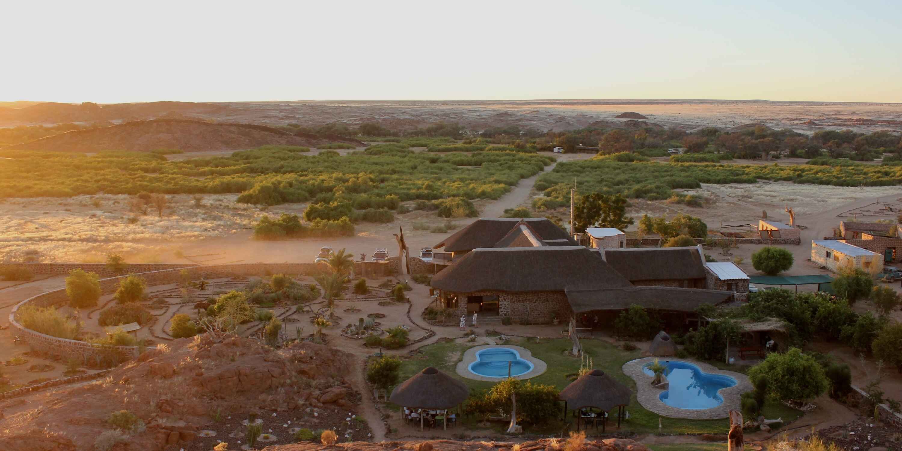 View looking down on a lodge with swimming pools and gardens.