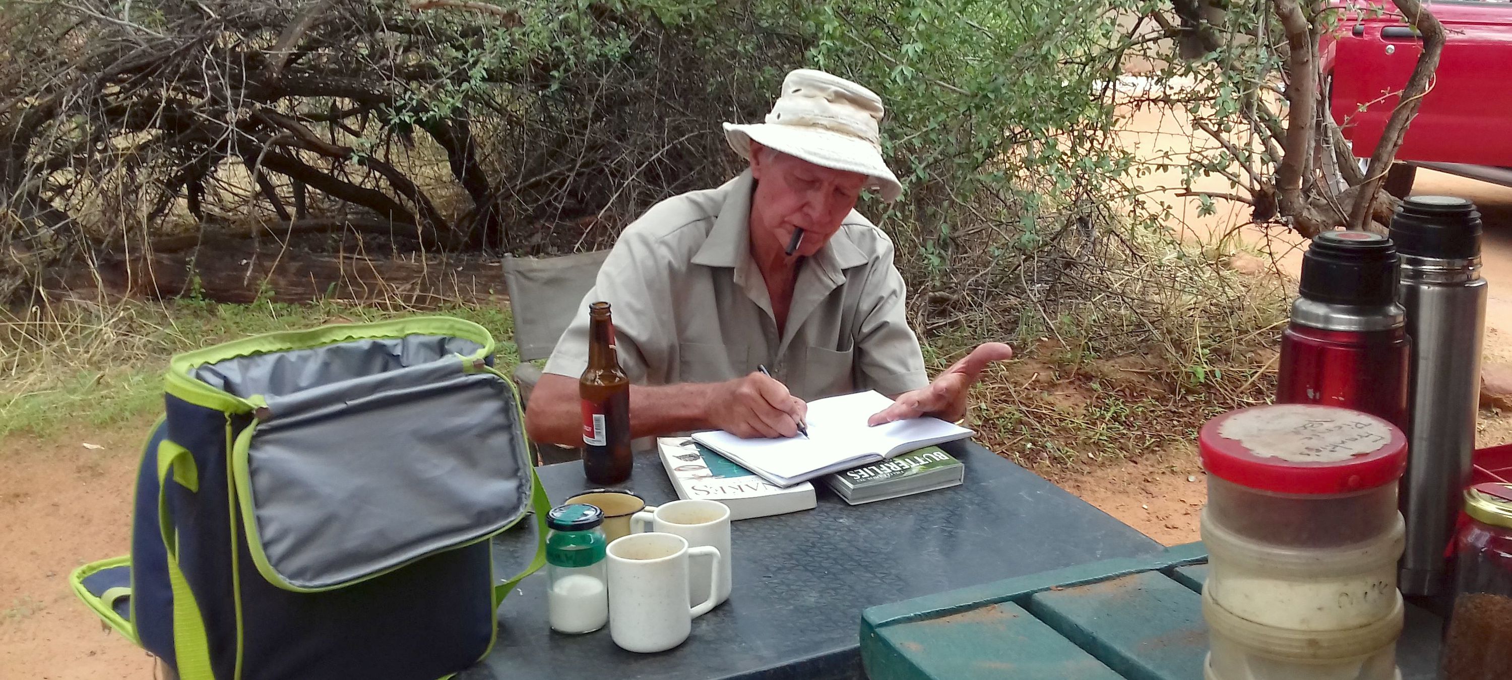 Dave Ward writing notes while sat at a camping table and surrounded by supplies.