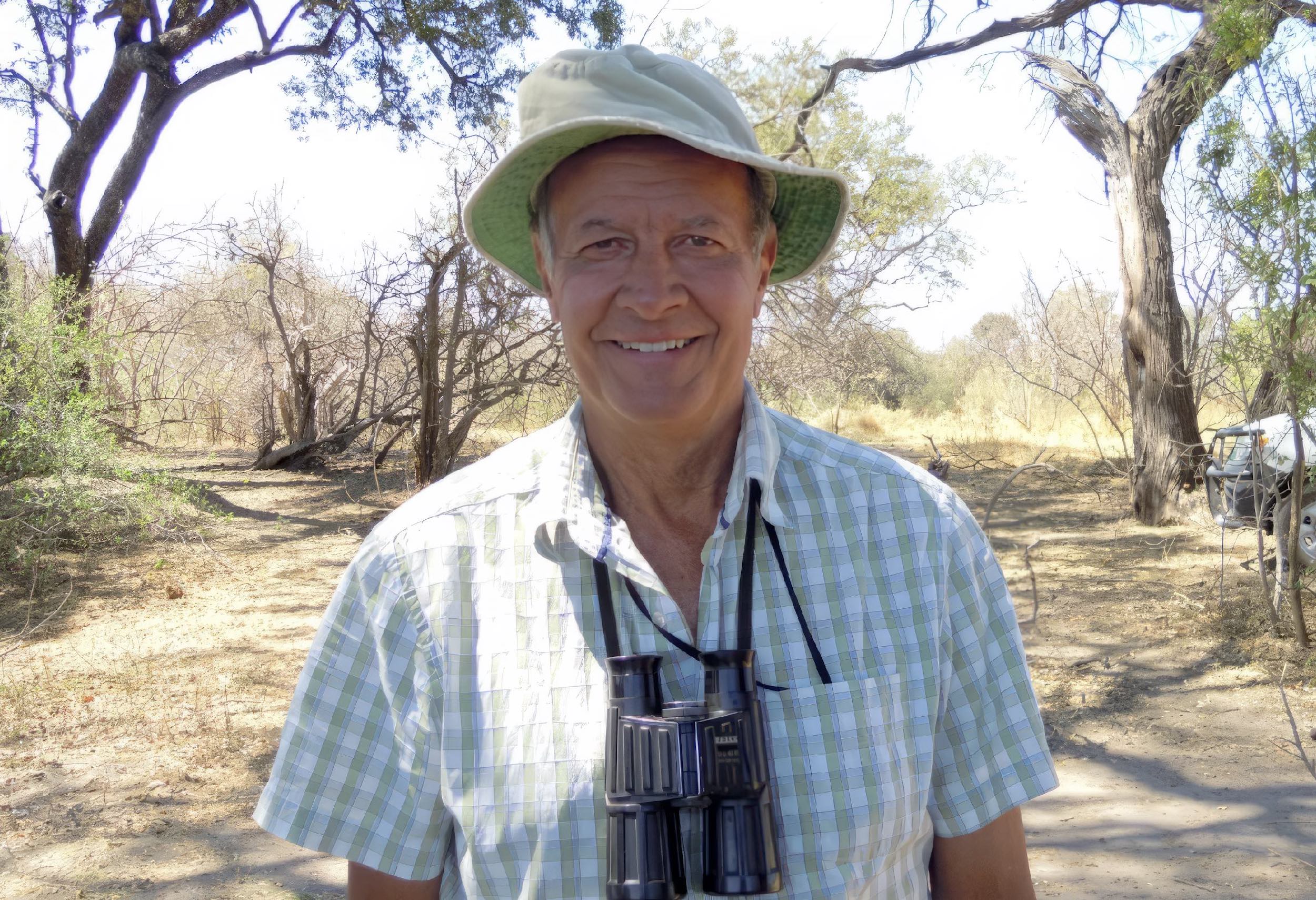 Dave Ward wearing a sunhat and with a pair of binoculars around his neck, smiling at the camera.