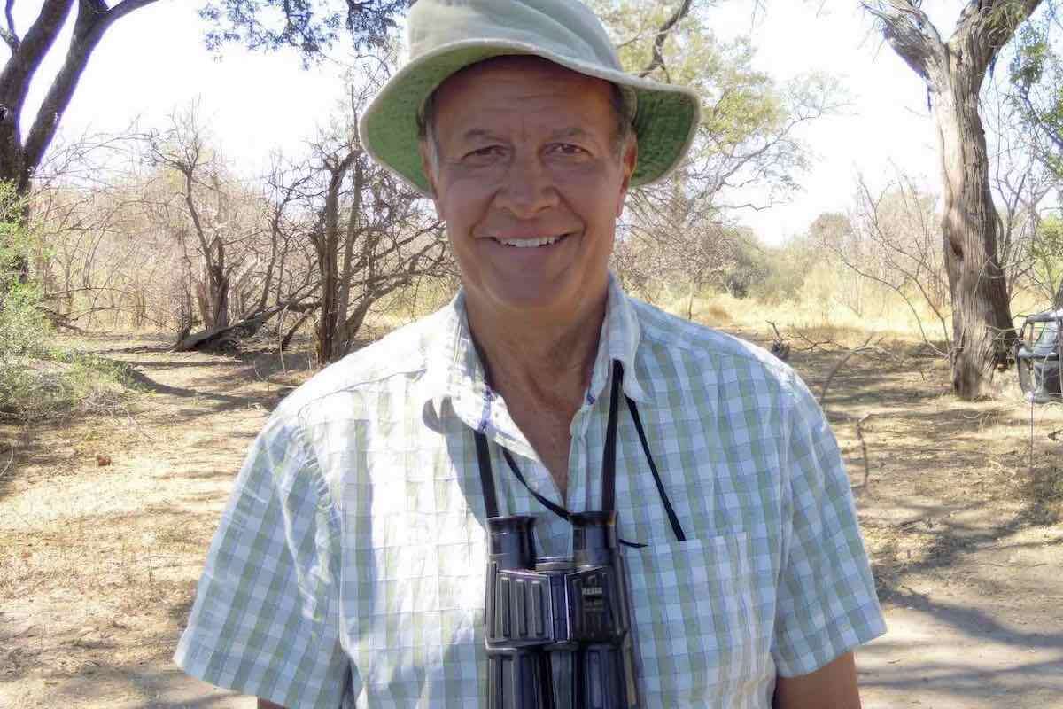 Dave Ward wearing a sunhat and with a pair of binoculars around his neck, smiling at the camera.