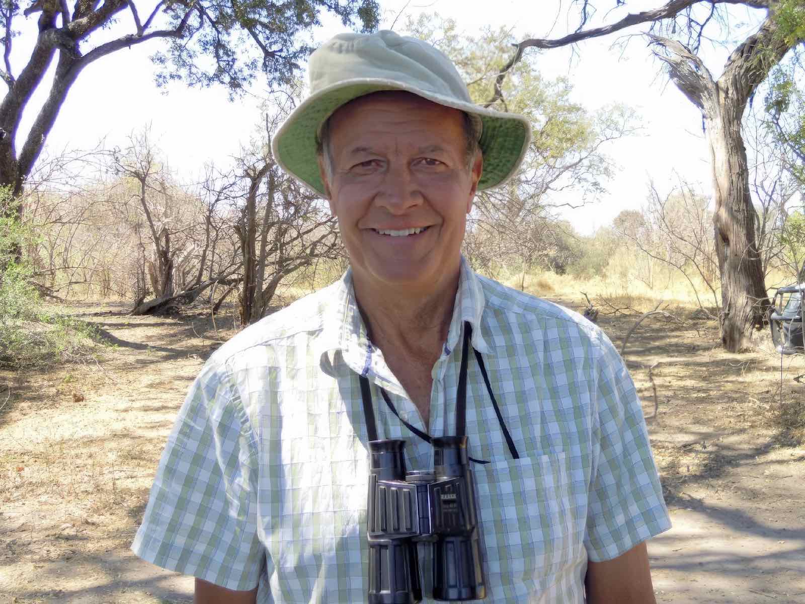 Dave Ward wearing a sunhat and with a pair of binoculars around his neck, smiling at the camera.