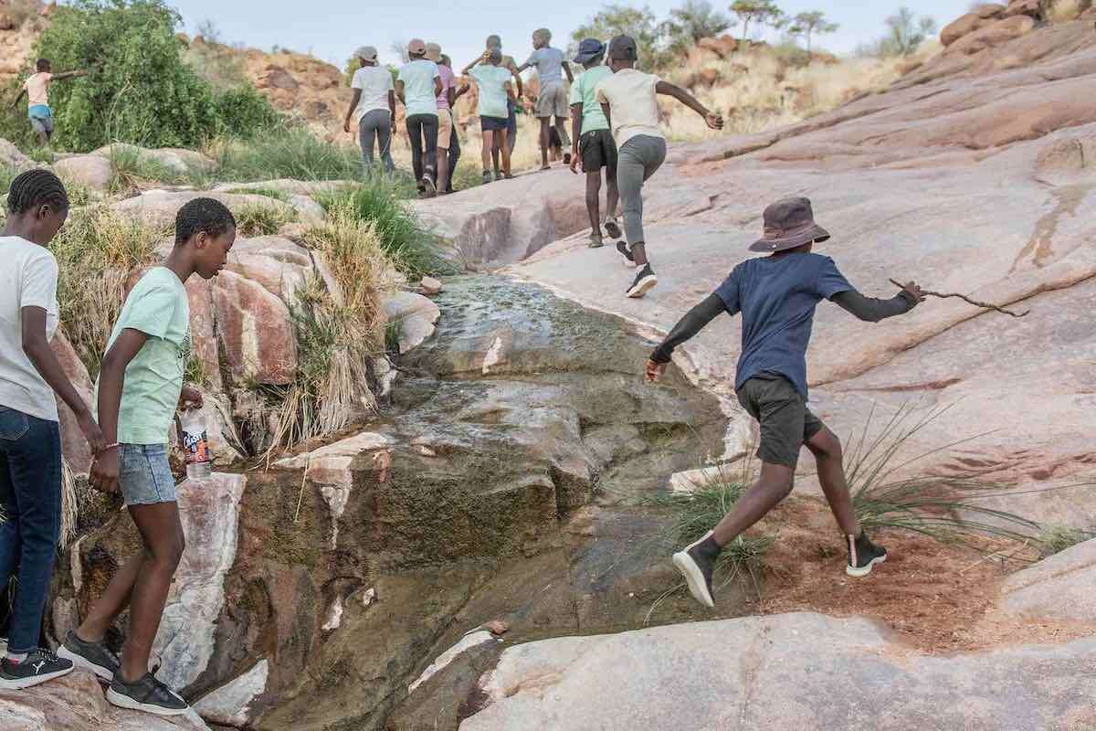 A group of children scramble up a rocky riverbed.