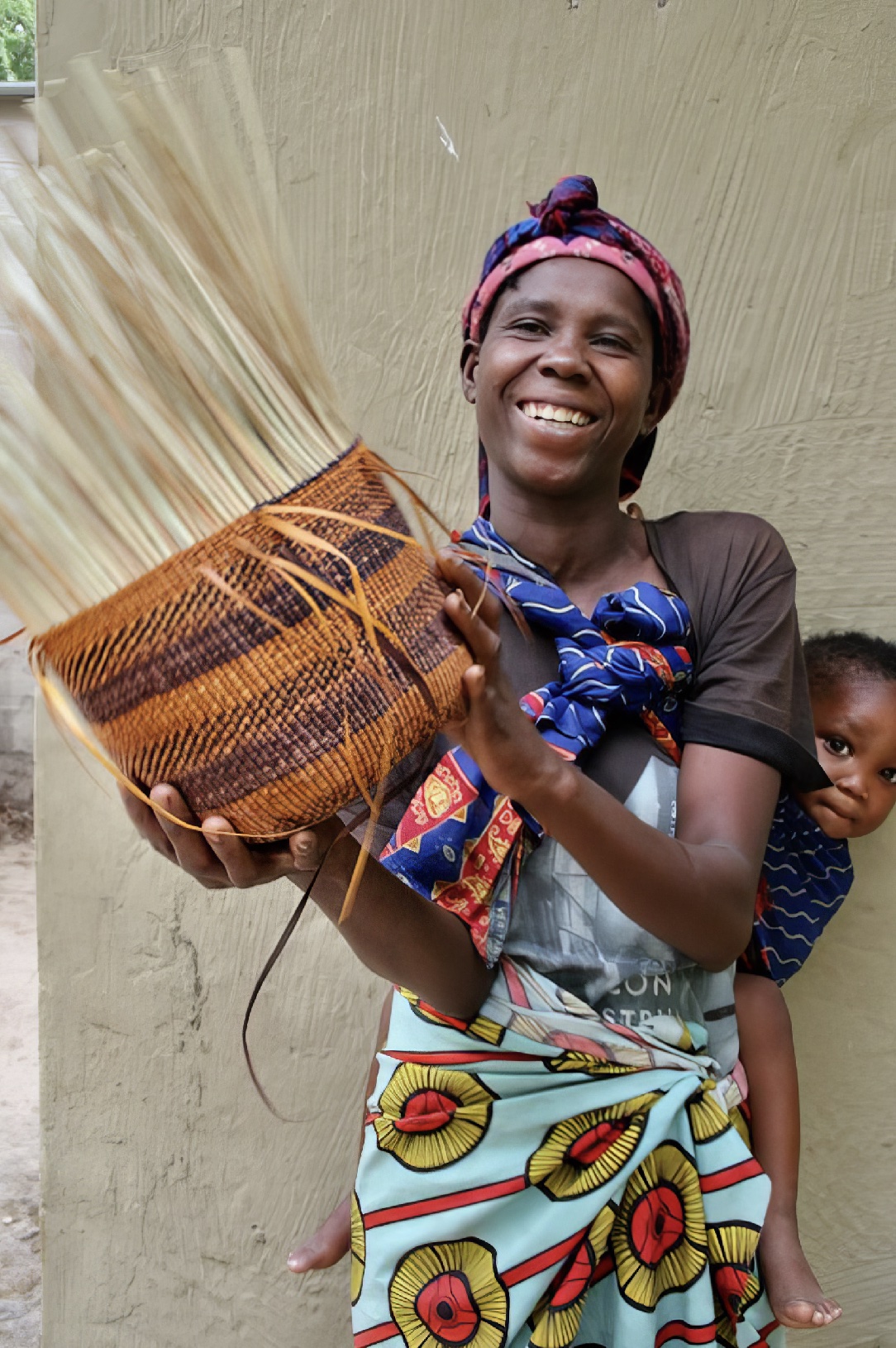 A San woman holding her partly woven basket, while a small child peers around her shoulder.