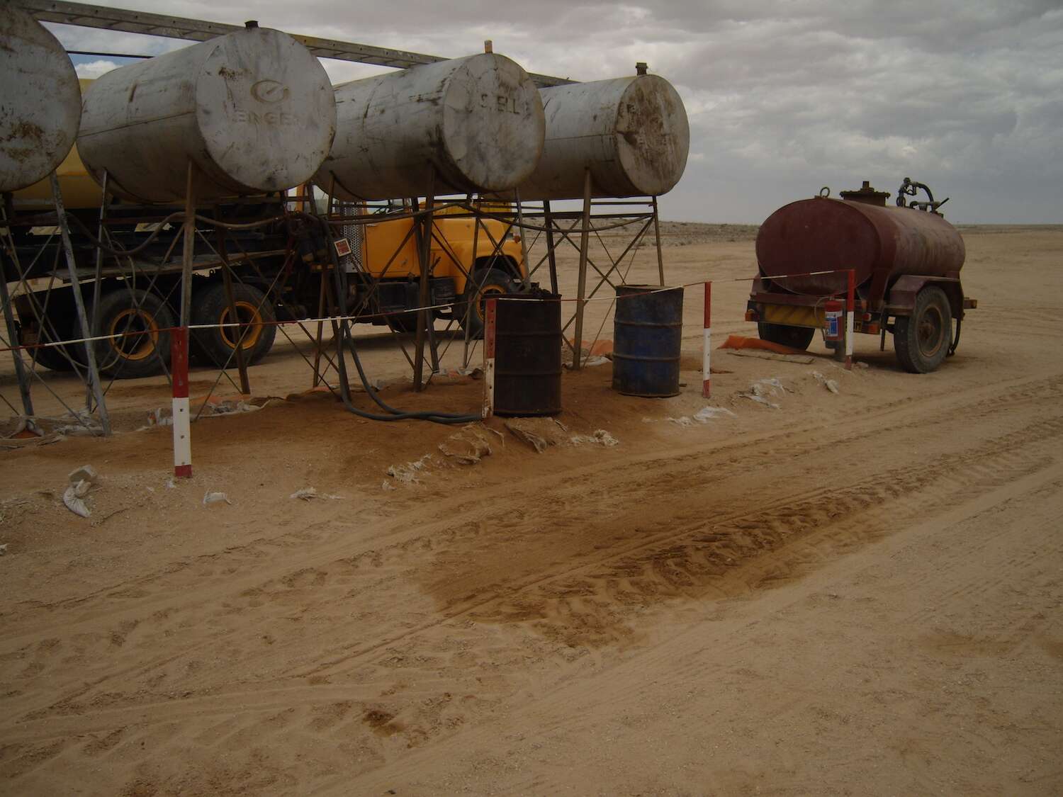 A line of fuel tanks above a spreading stain of spilt fuel in the desert.