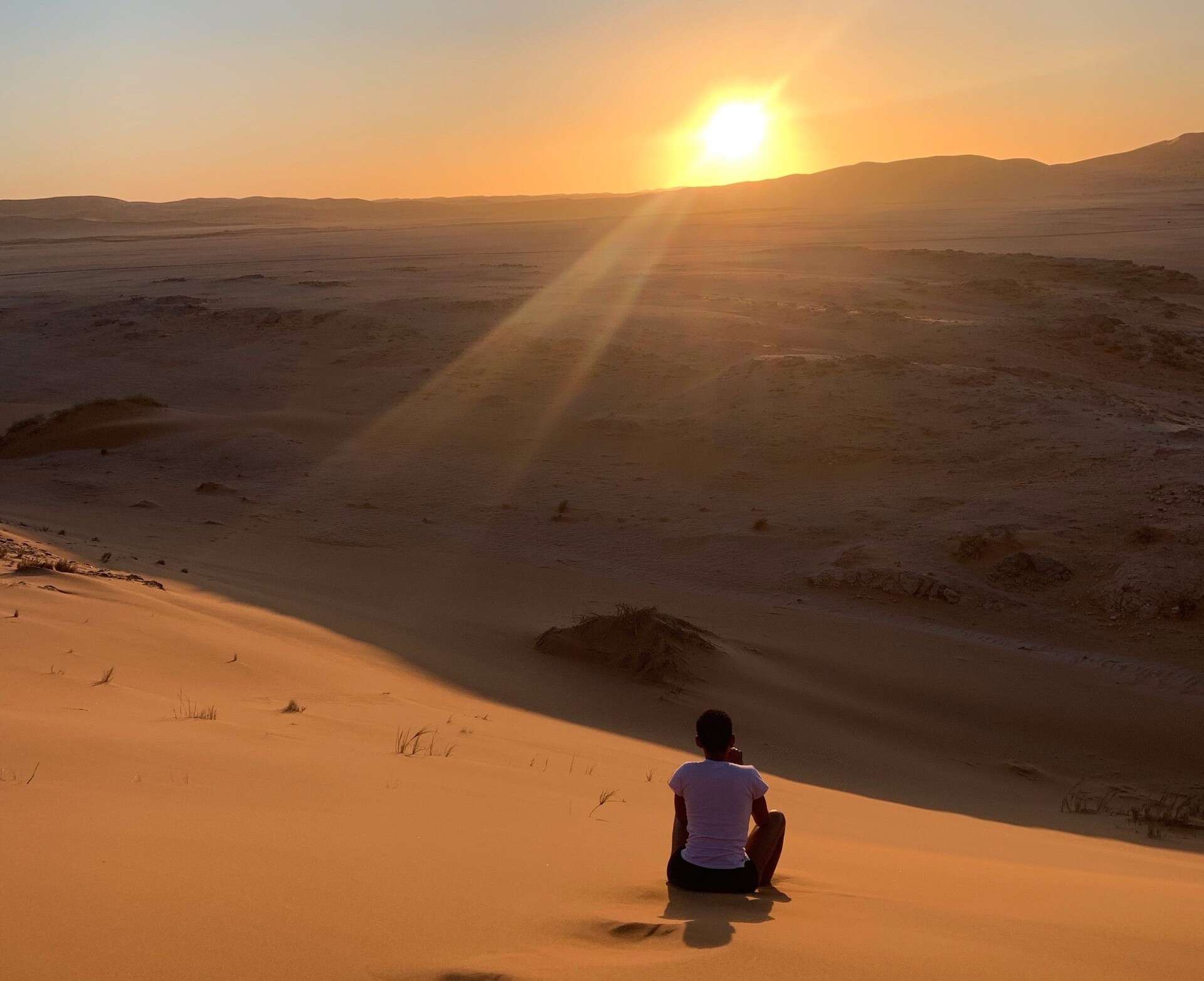 A young woman watching the sun low on the horizon in the desert.