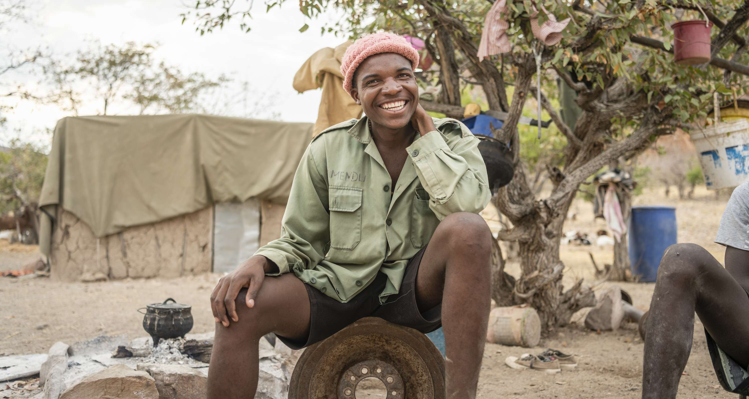 A smiling man sits on an old wheel hub.