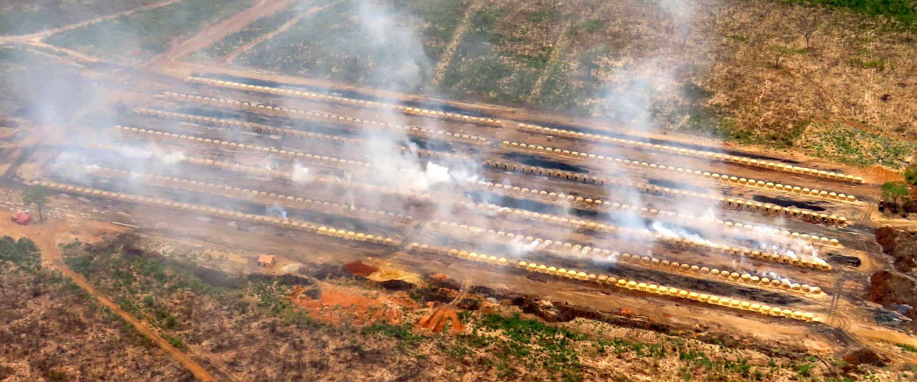 Smoke rises from lines of small circular structures filling a field.