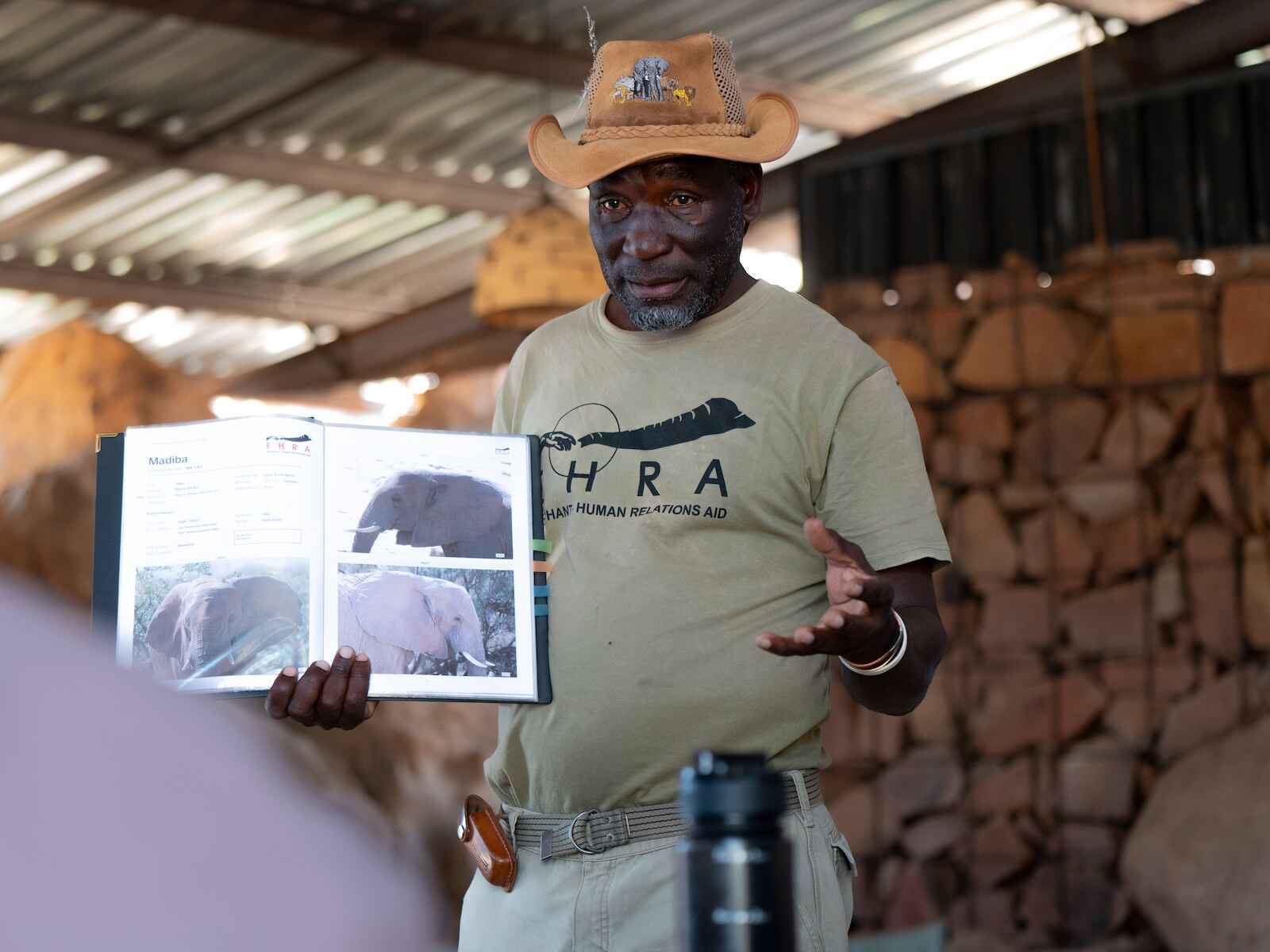 A man holding open a booklet and facing a group in a classrom setting.