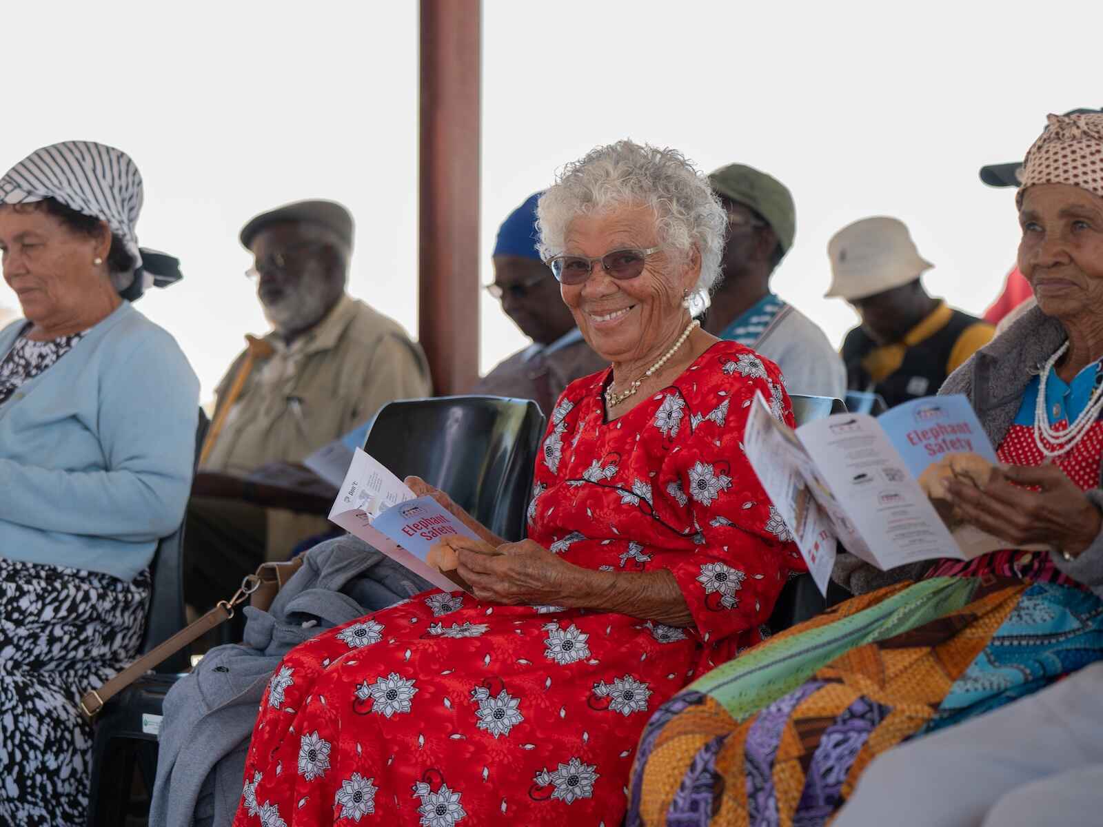 Community members sitting on plastic chairs and paging through booklets.