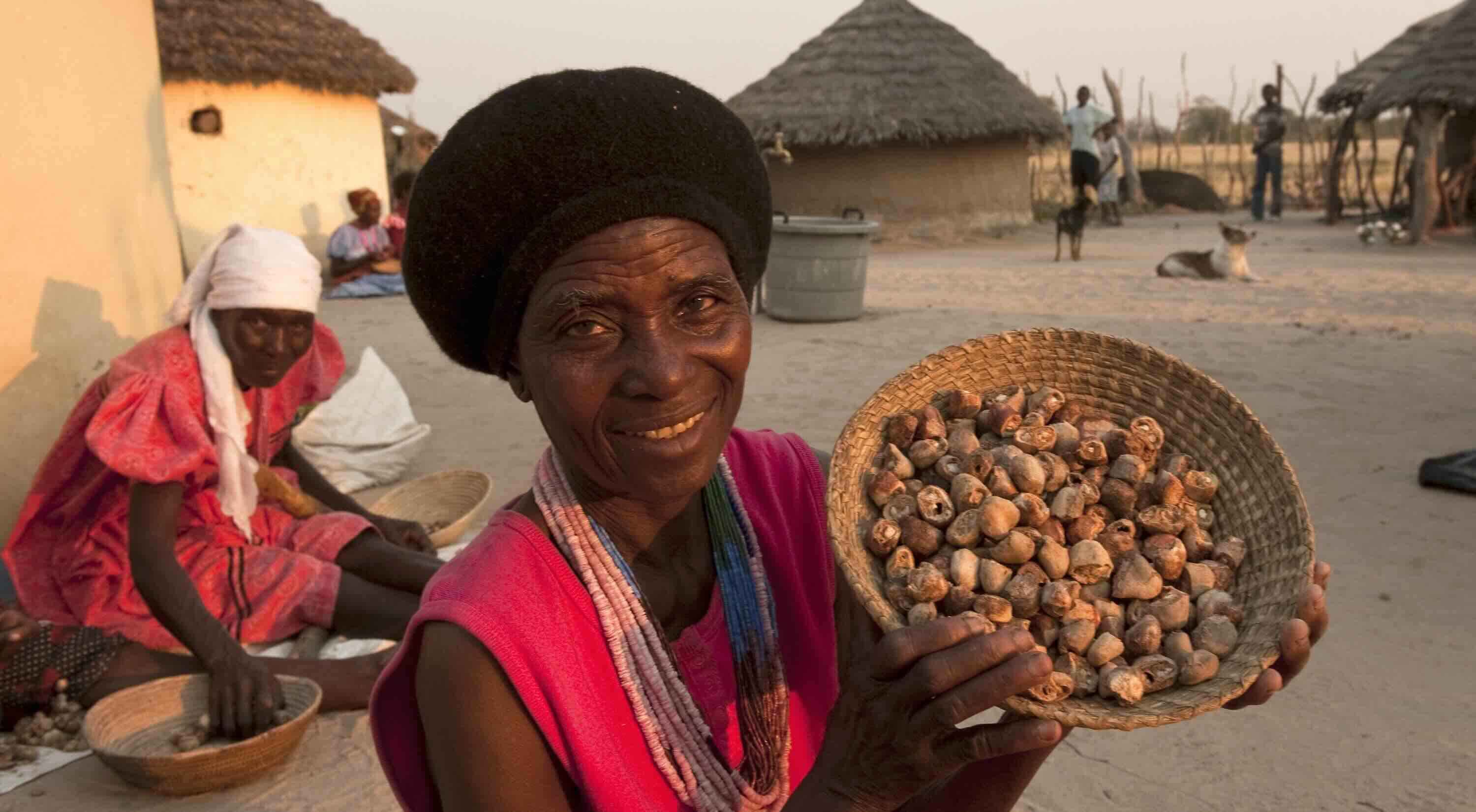 A smiling woman shows a basket of dried marula.