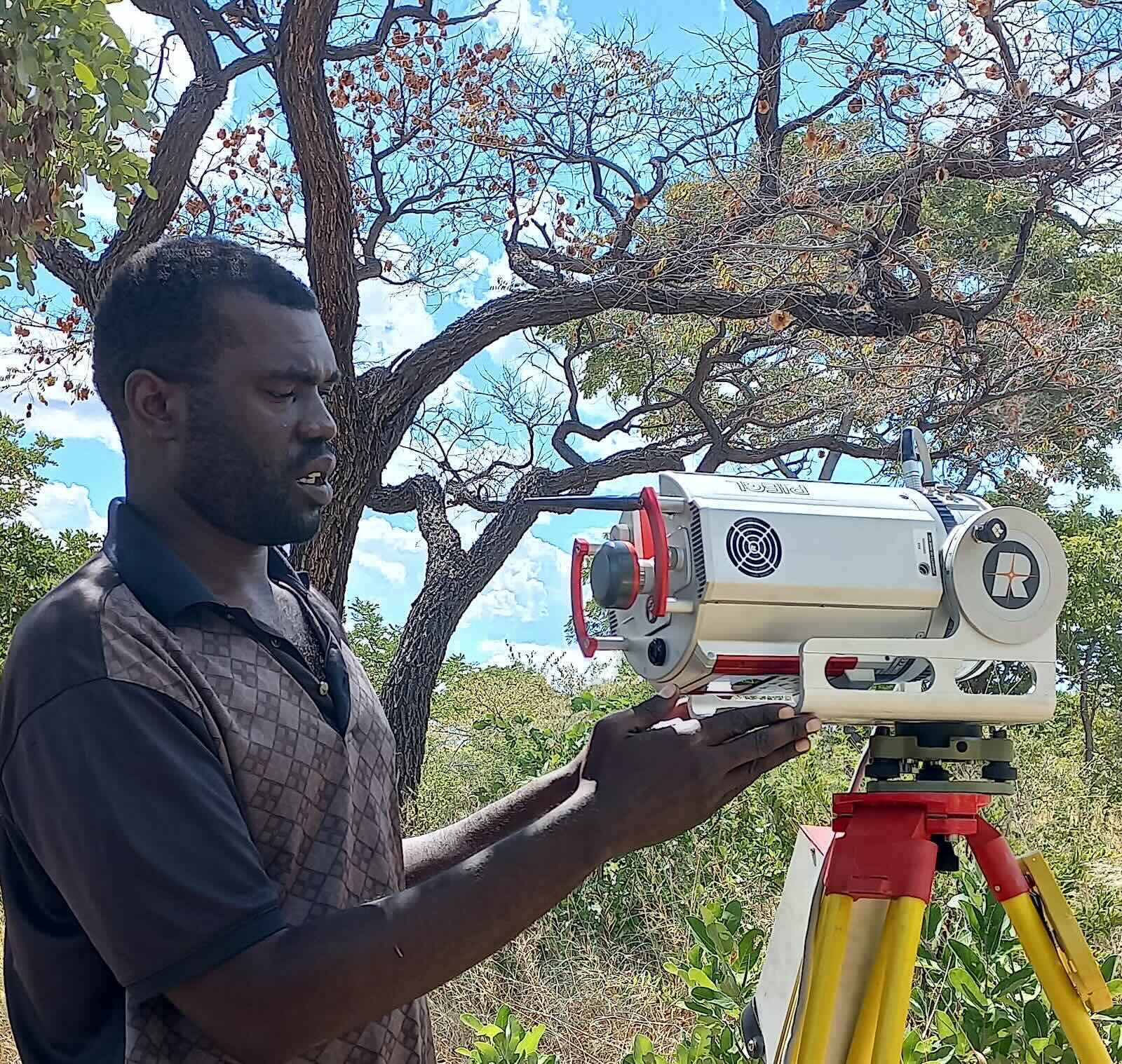 A man adjusting settings on an instrument on a tripod while in a thick forest.