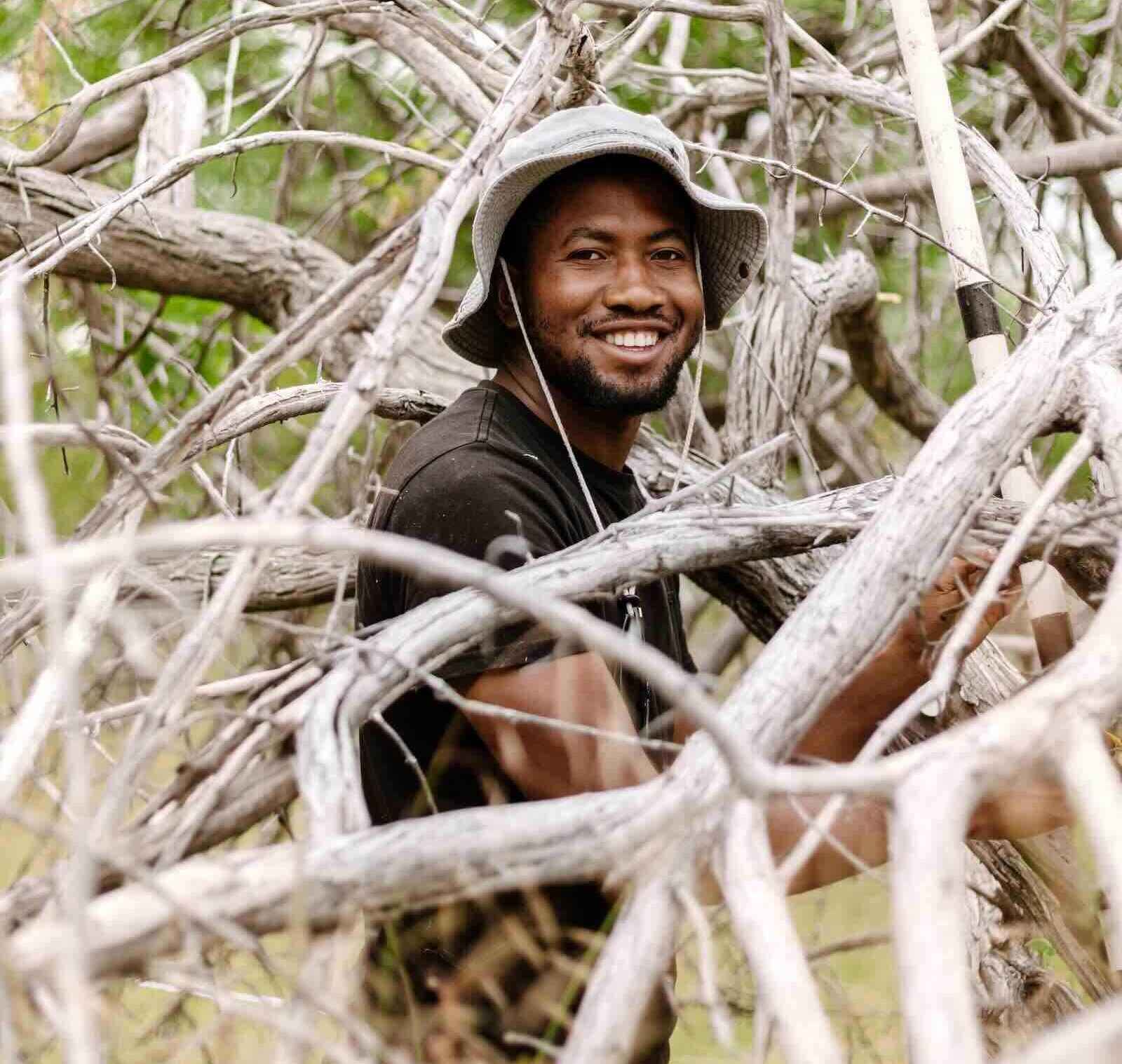 Gabriel Uusiku stands among many branches and smiles for the camera.