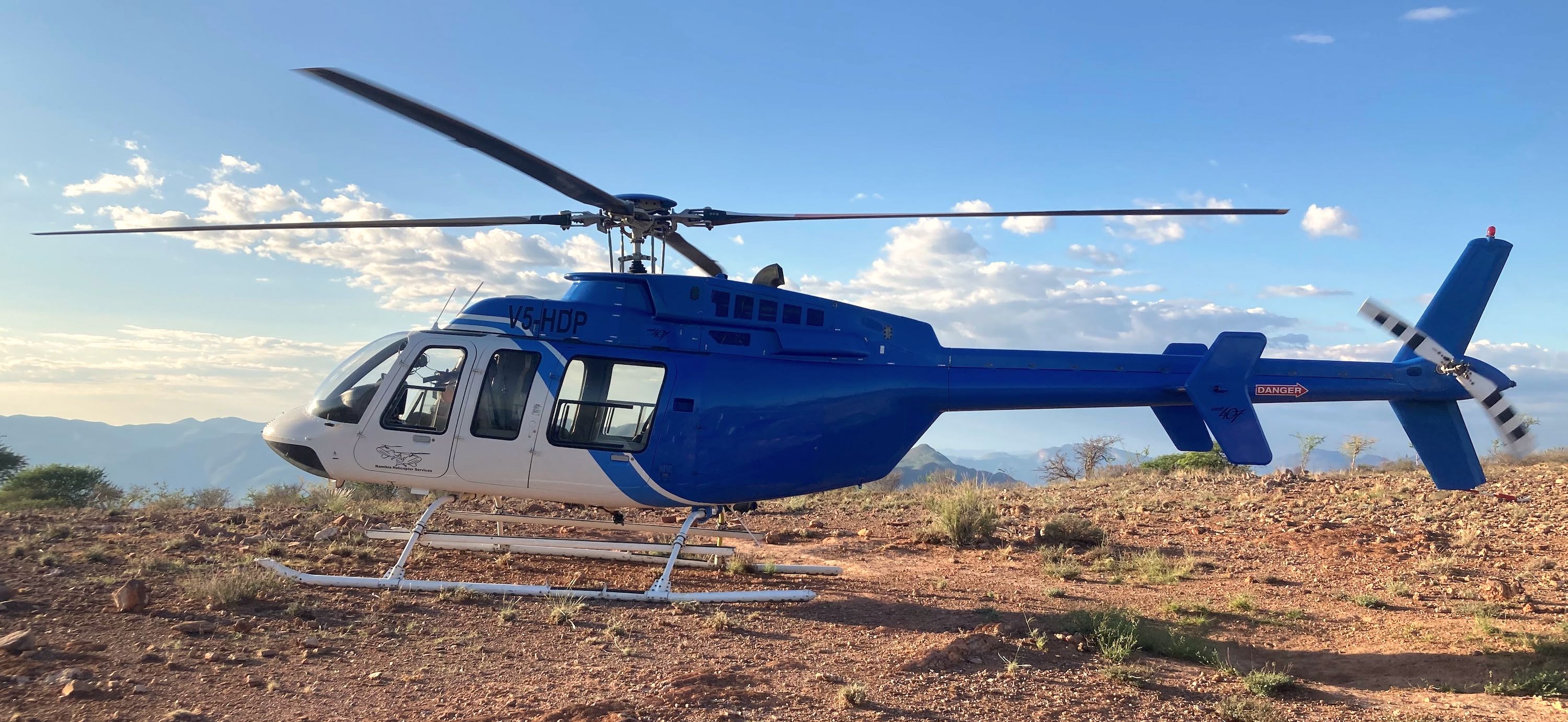 A blue and white helicopter prepares to take off from a high plateau.