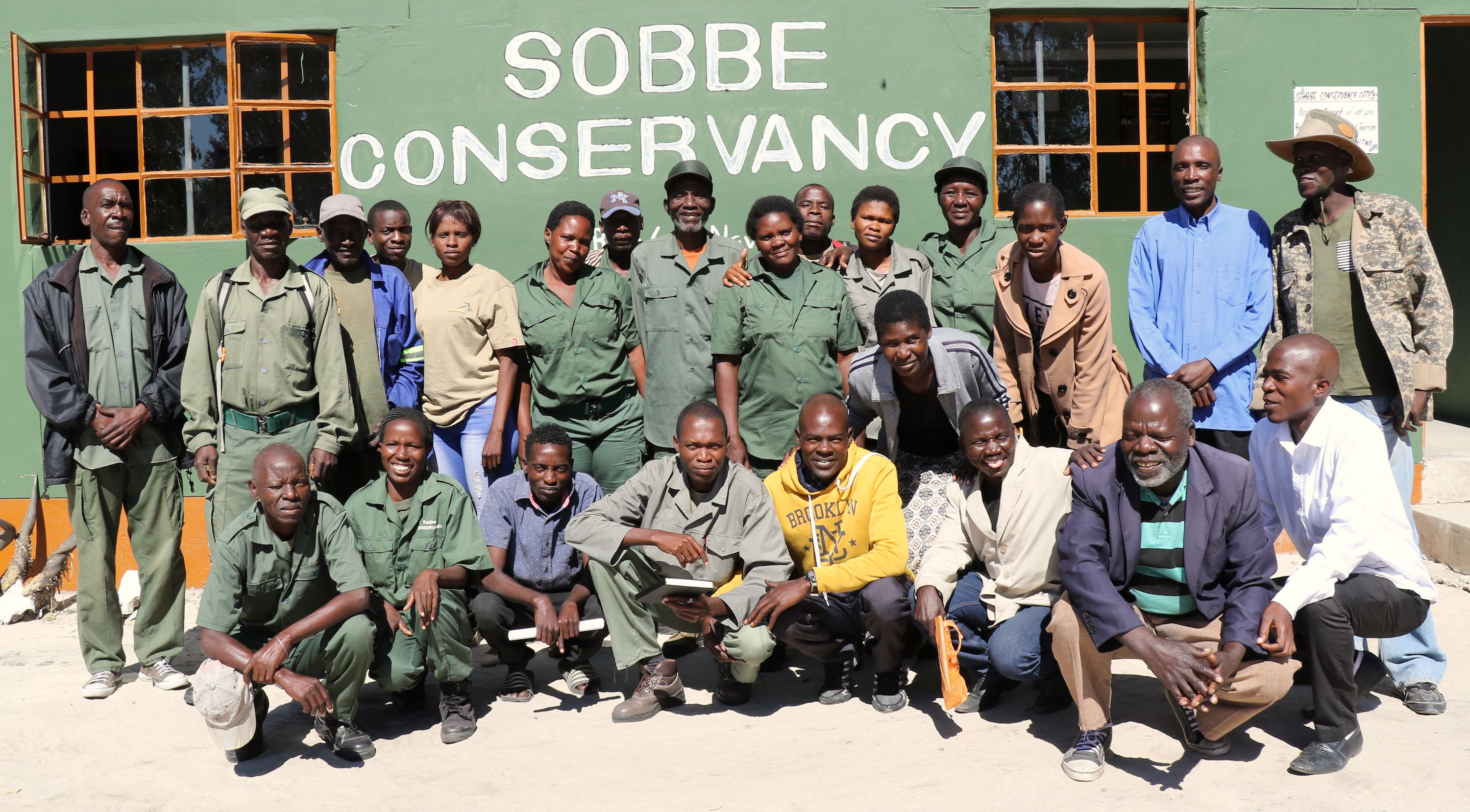 A group photograph showing the men and women of the Sobbe Conservancy committee posing outside of their office.