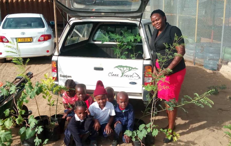A woman and several children standing next to a bakkie filled with saplings.