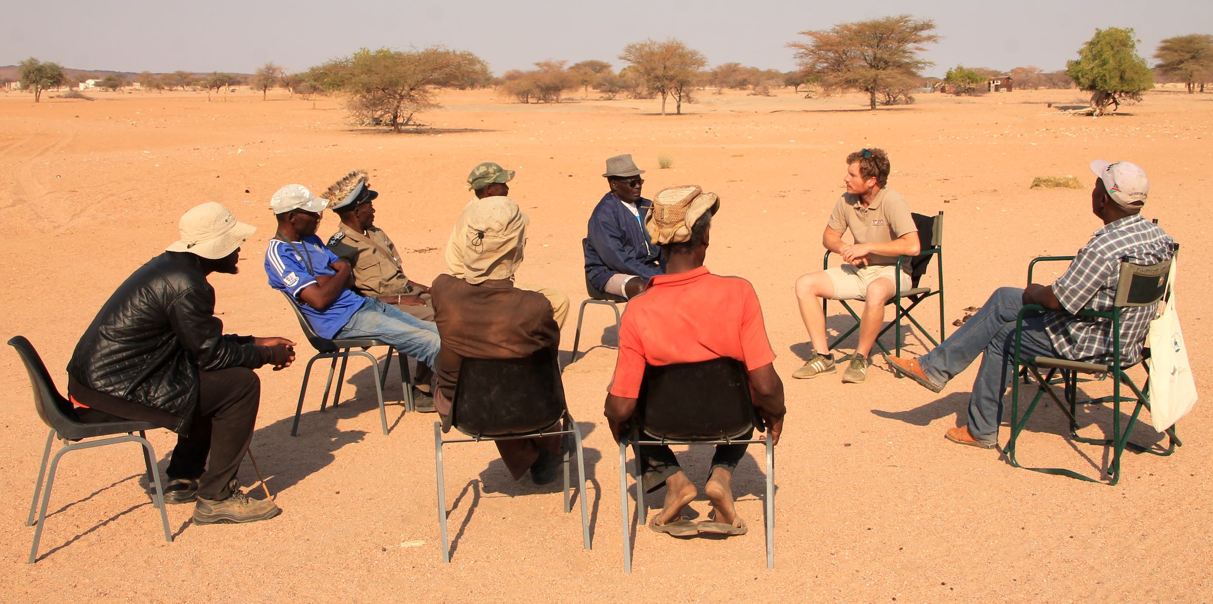 A group of people sitting on a circle of chairs in the desert - a meeting with a view!