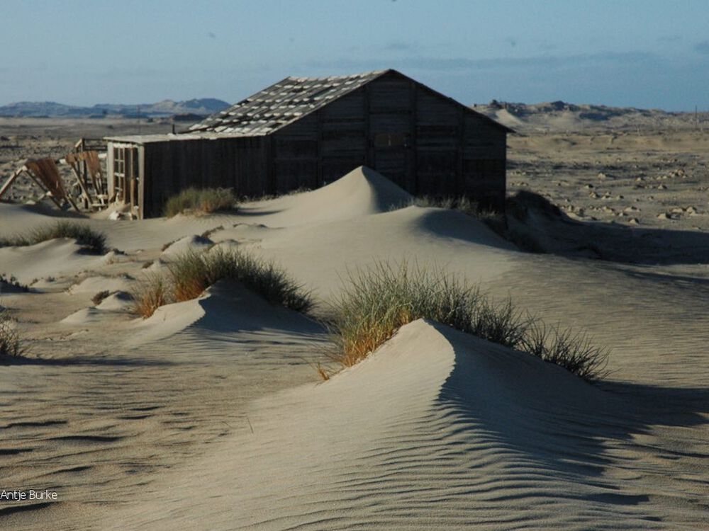 A sand dune merges with an old ruined house.