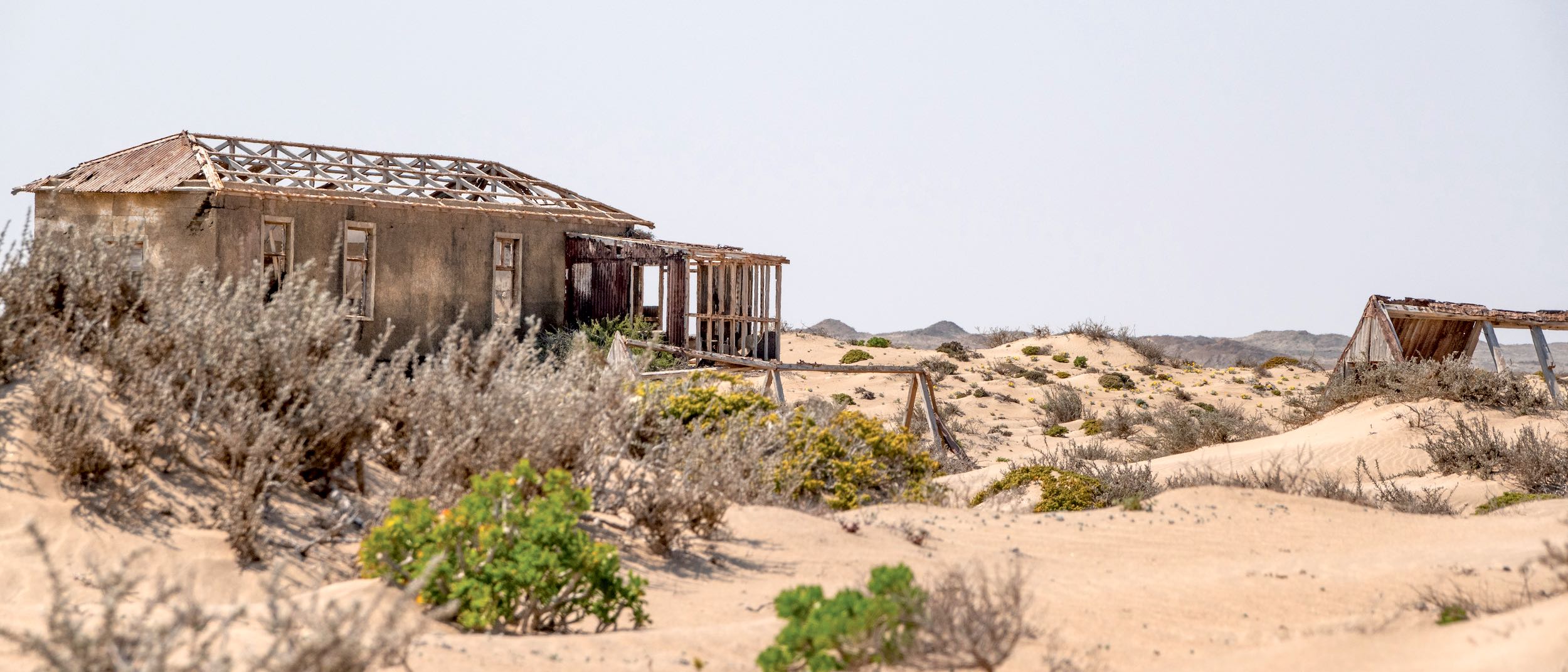 A pair of single story buildings decay as the desert encroaches.