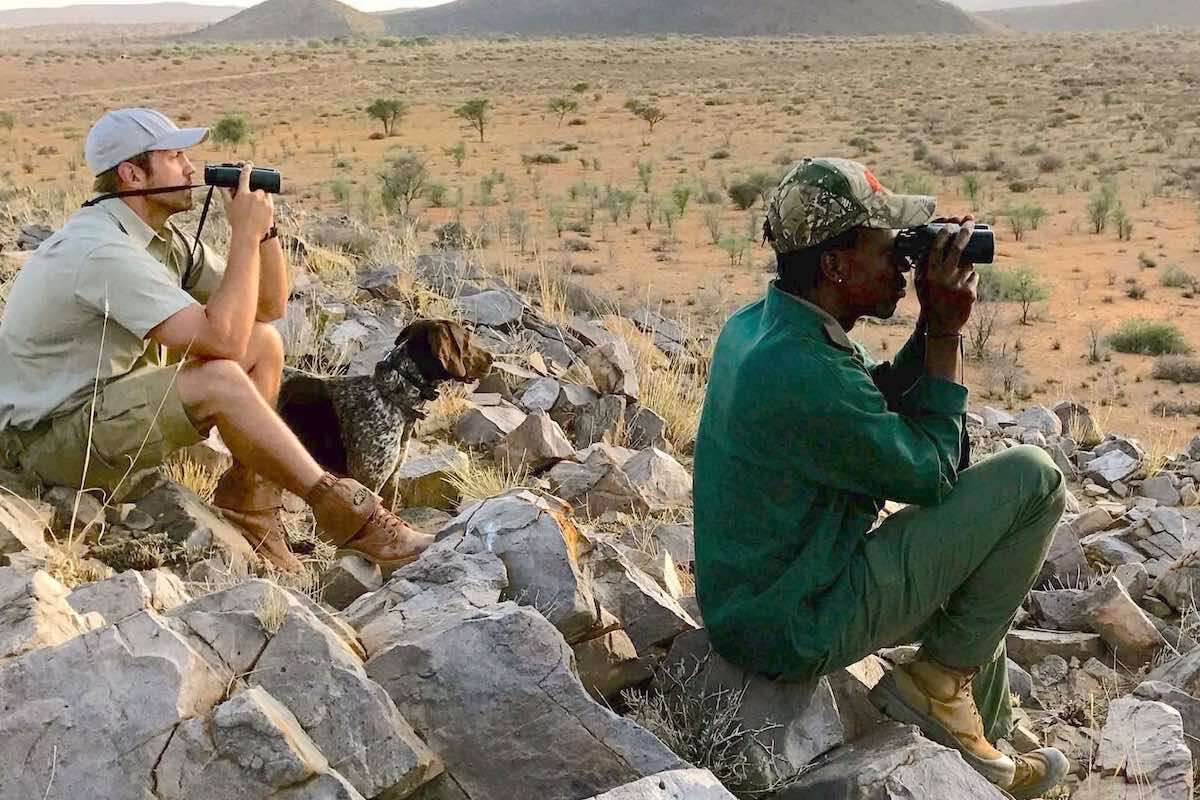 A hunter, his guide, and a dog, stare into the distance looking for wildlife.