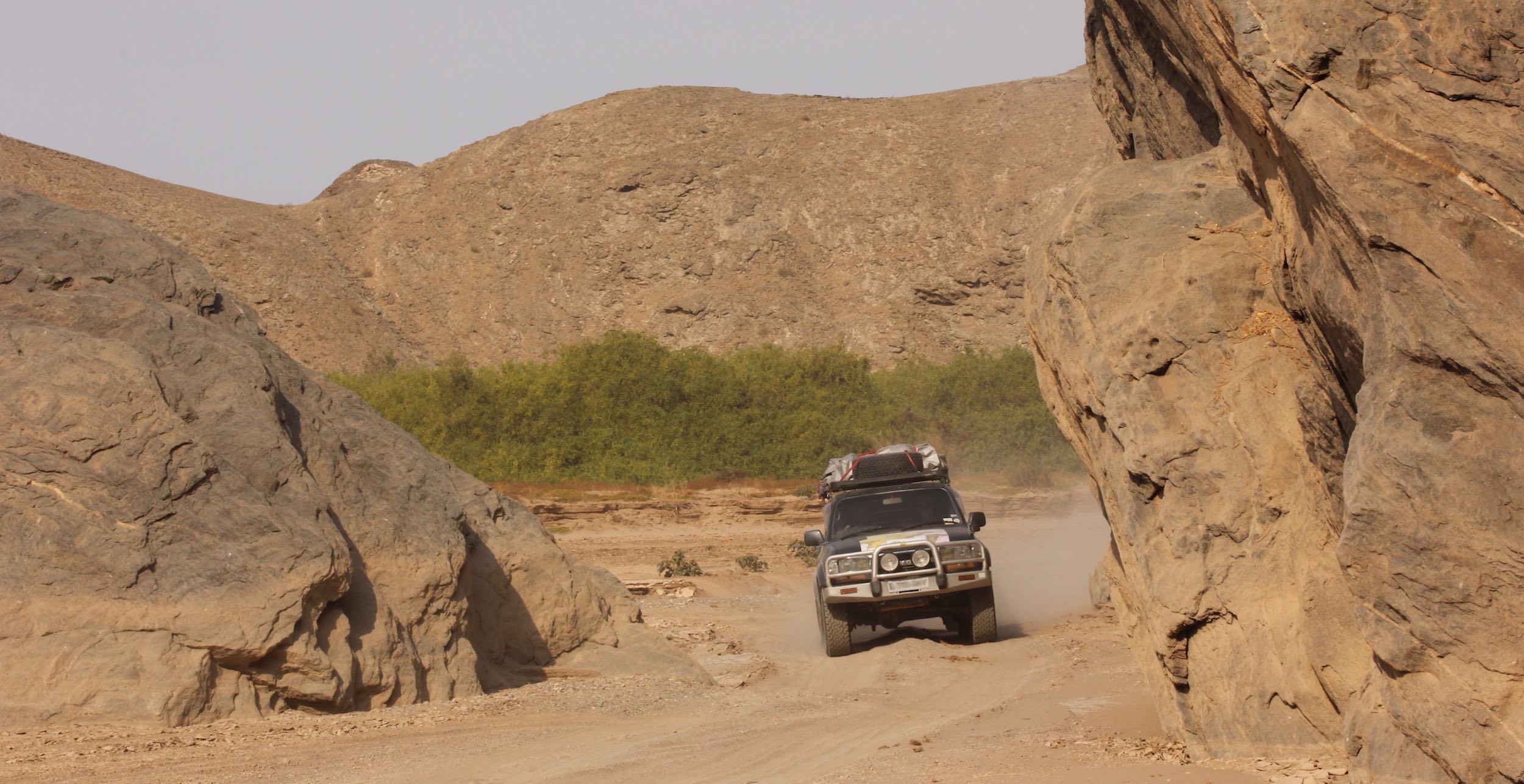 A landcruiser drives through thick sand along a dry riverbed in northern Namibia.