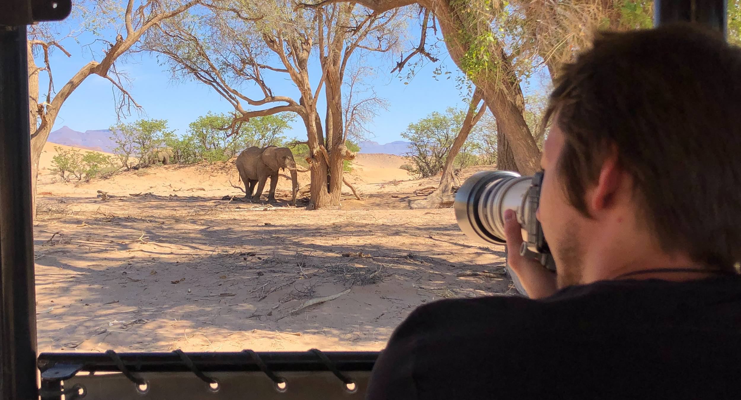 A tourist focusses a camera on an elephant from the safety of his vehicle.