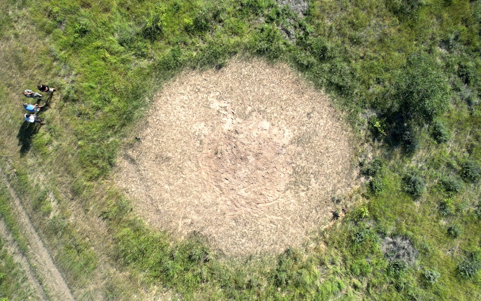 An aerial view of a Namibian fairy sphere with four people standing next to it.