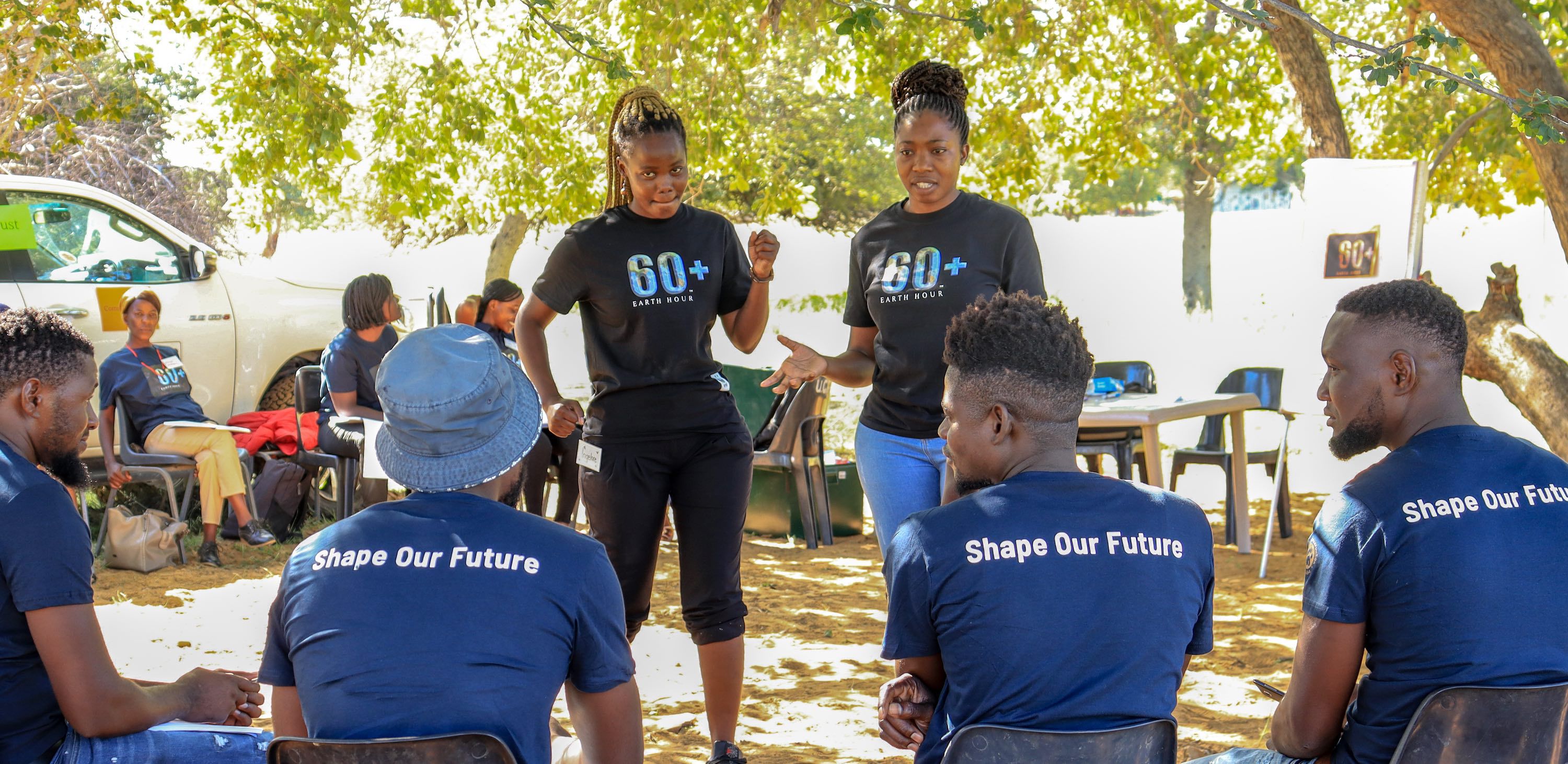 Two young women addressing a group wearing Shape Our Future t-shirts