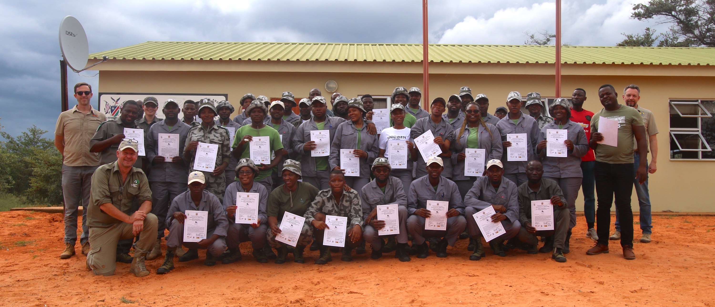 A group of rangers pose for a photograph outside a single story building.